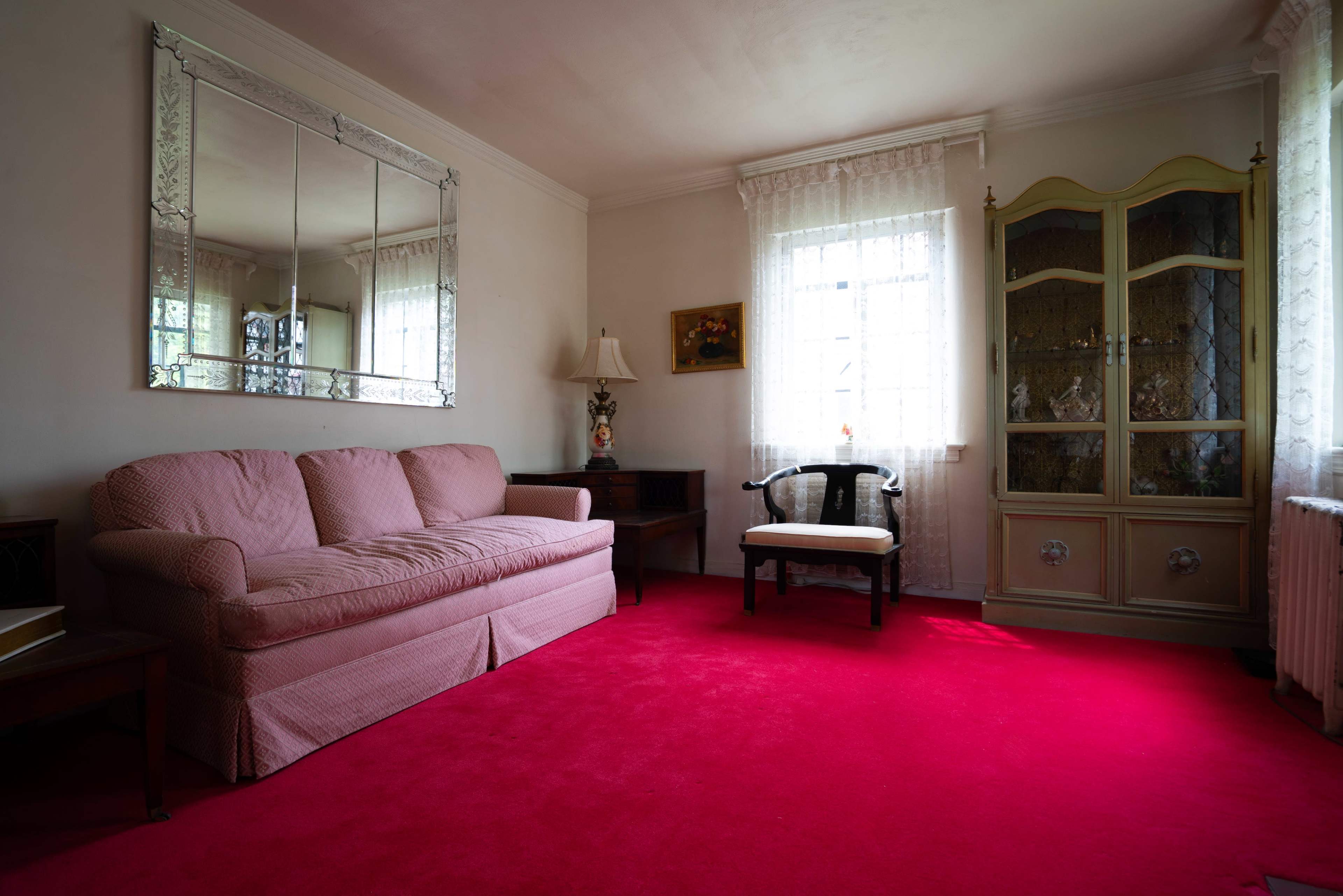 The image shows a living room with a pink sofa, a black chair, a cabinet, and bright pink carpet.