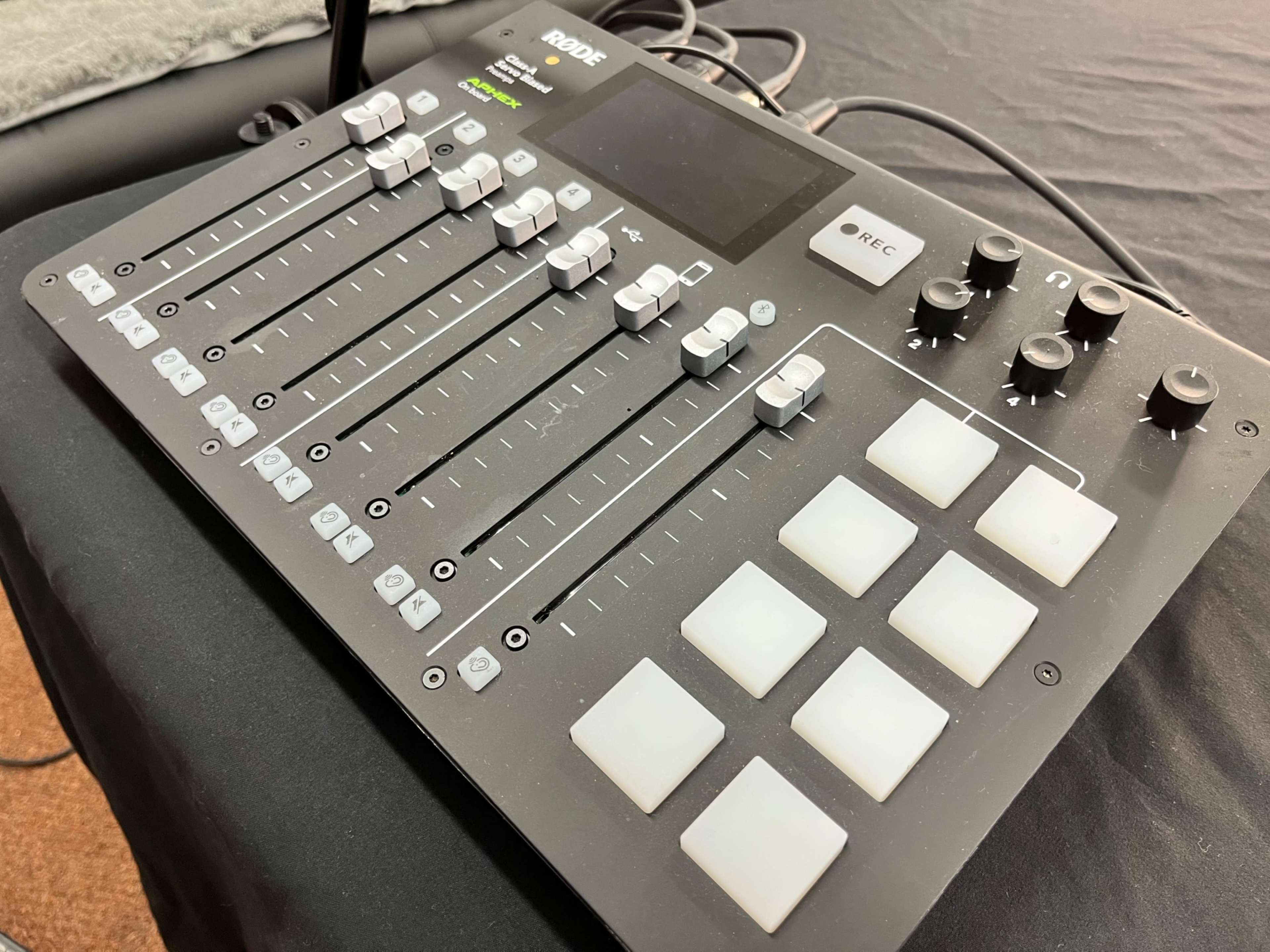 A RODE audio mixer featuring faders, buttons, and knobs arranged in a grid layout on a black surface.
