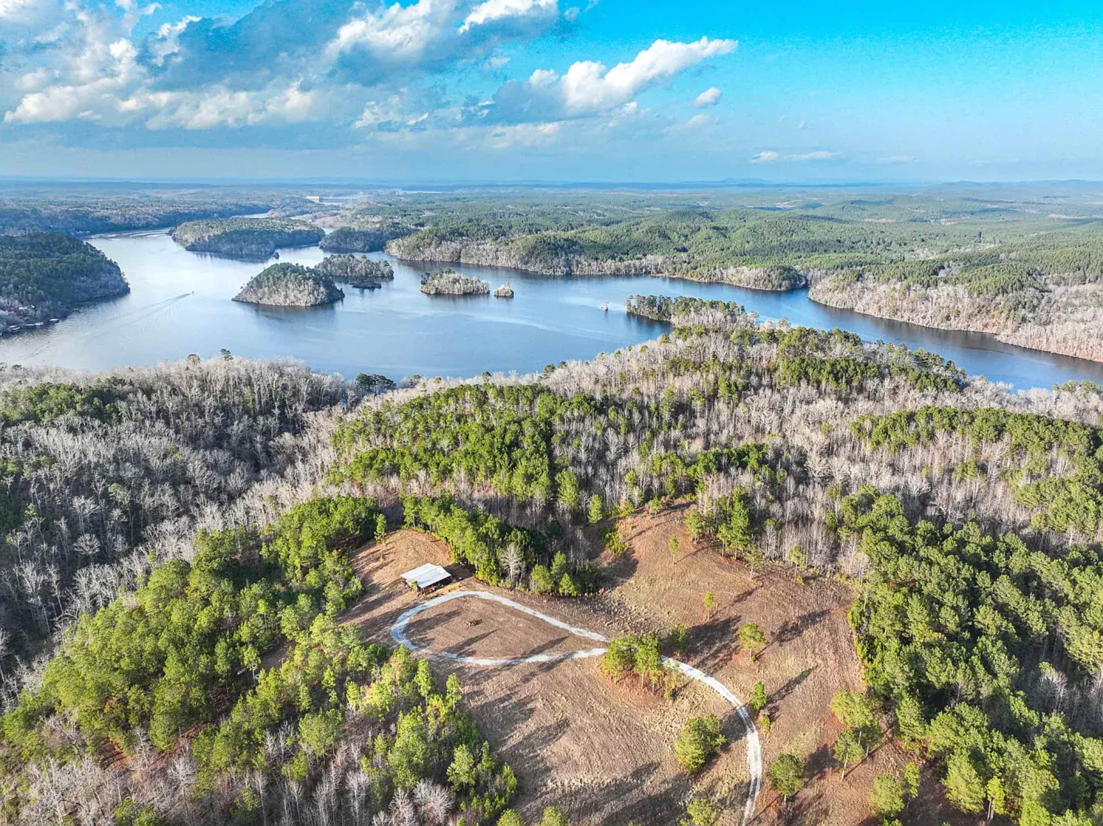 The image shows a wide aerial view of a lake surrounded by dense forests and hilly terrain, with several small islands in the water.