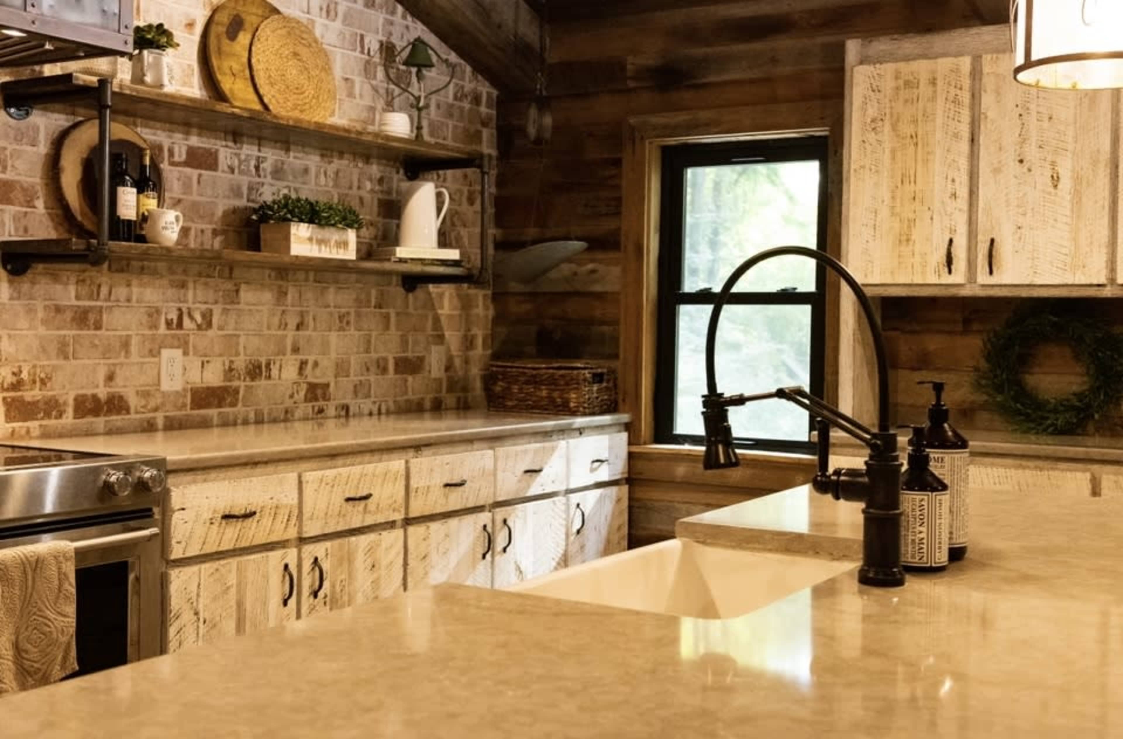 A rustic kitchen with wooden cabinetry, open shelving, and a large window that lets in natural light.