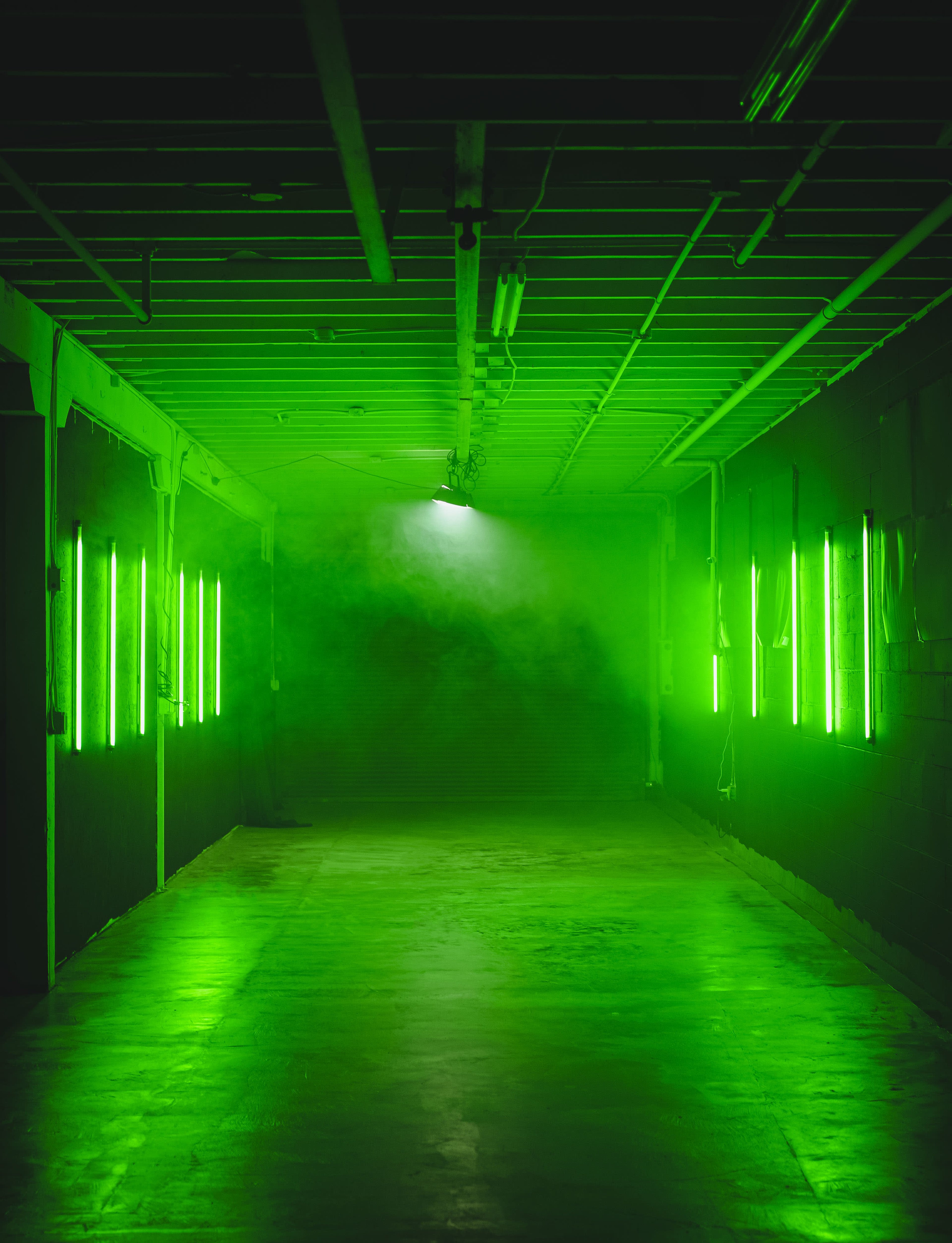 A dimly lit corridor is illuminated by green neon lights along the walls, with a foggy ambiance creating a mysterious atmosphere.