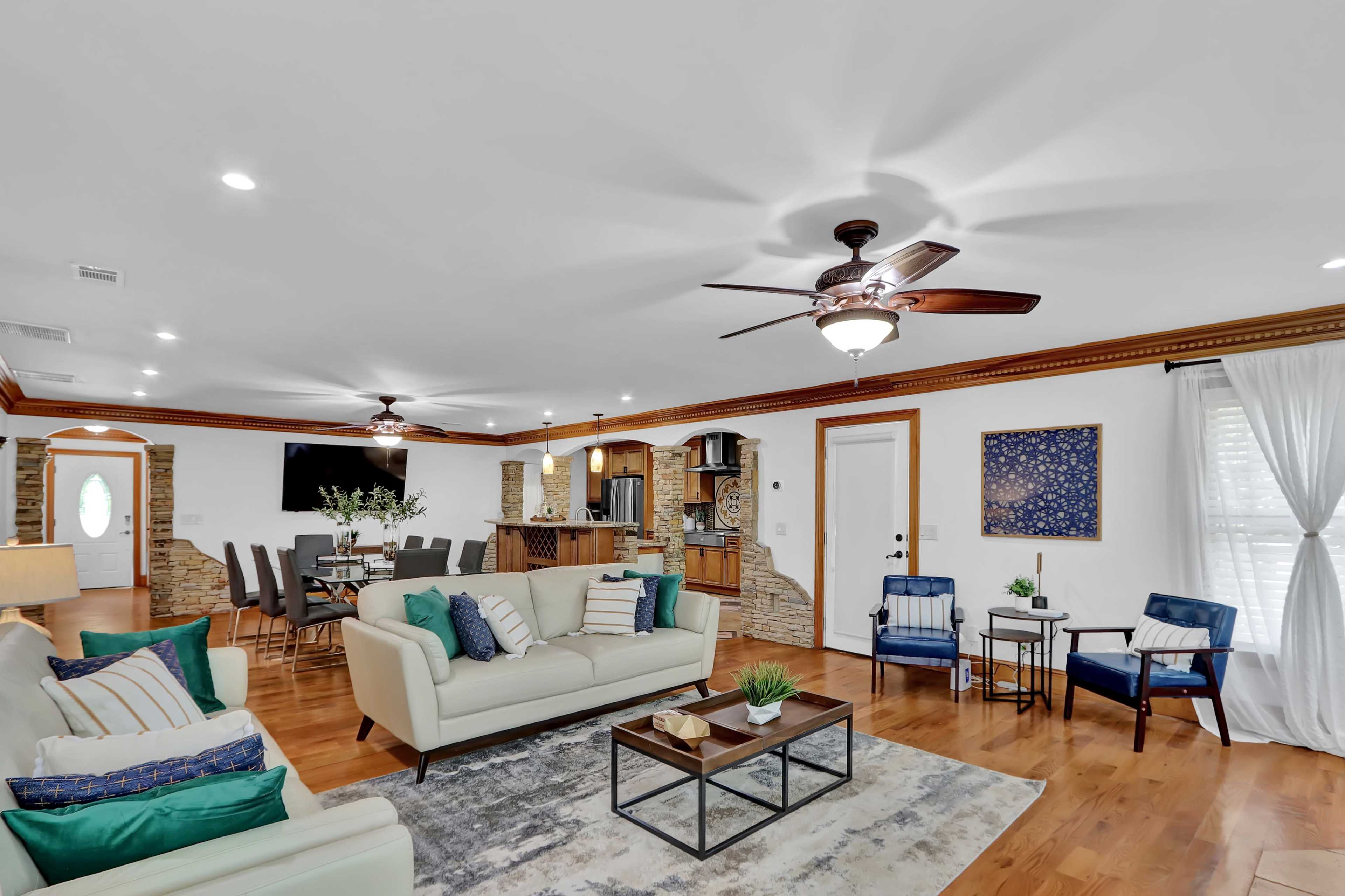 A spacious living room with a light-colored sofa, wooden flooring, and a kitchen area featuring a bar and stools in the background.