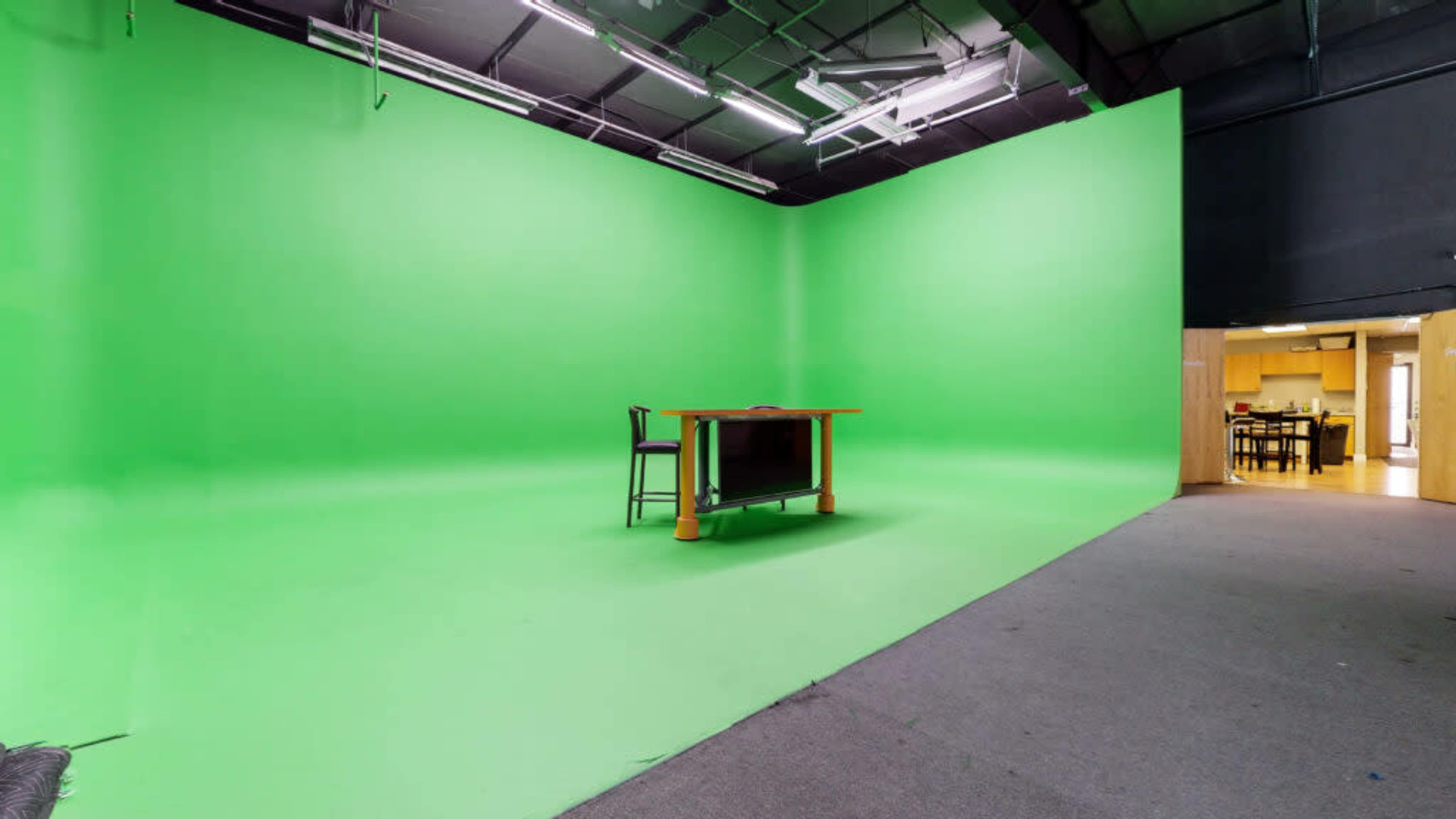 A large green screen studio with a table and chair set against a vibrant green backdrop.