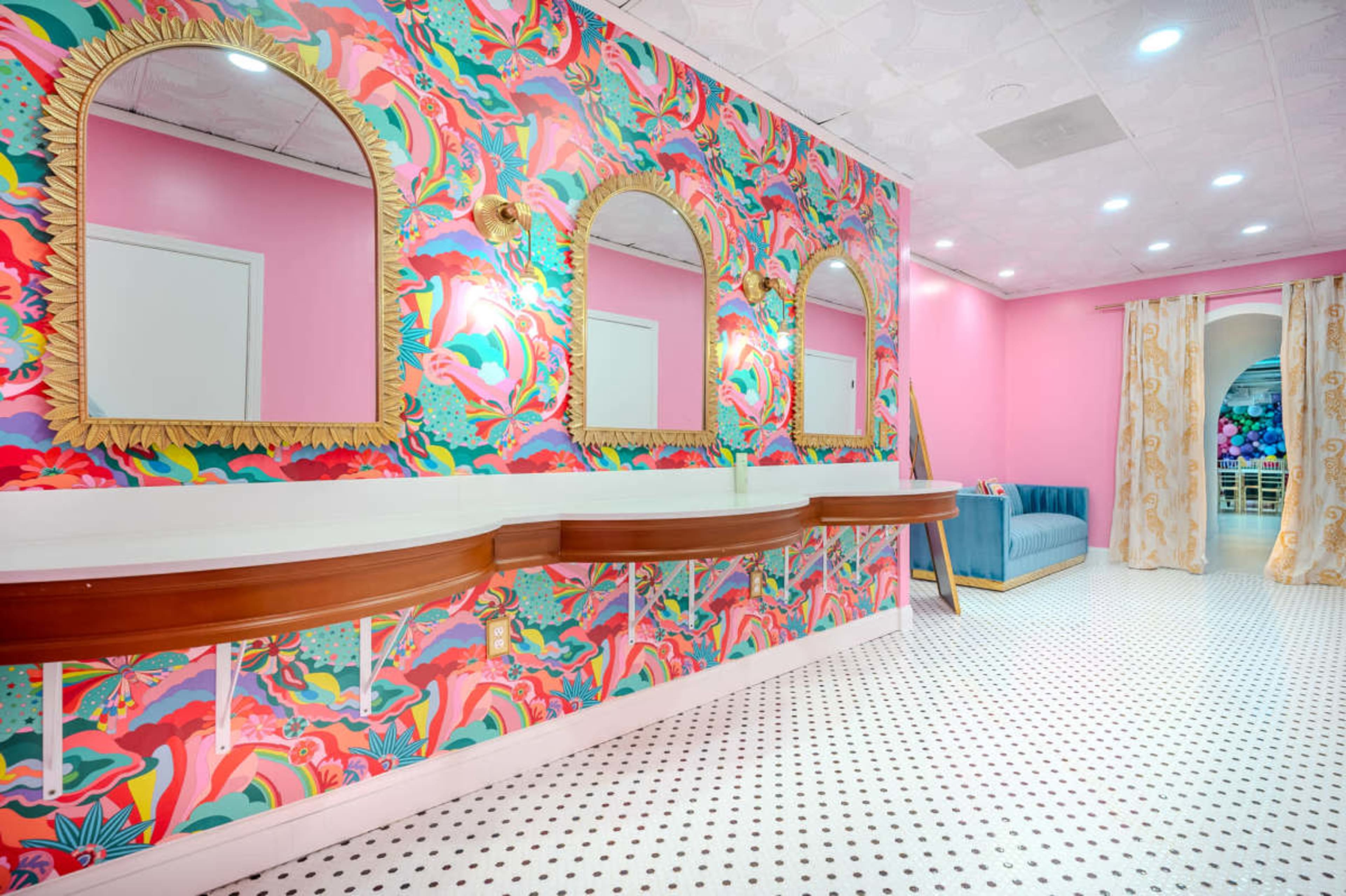 The image shows a brightly colored room with floral wallpaper, multiple arch-shaped mirrors, and a pink couch, featuring a patterned floor.