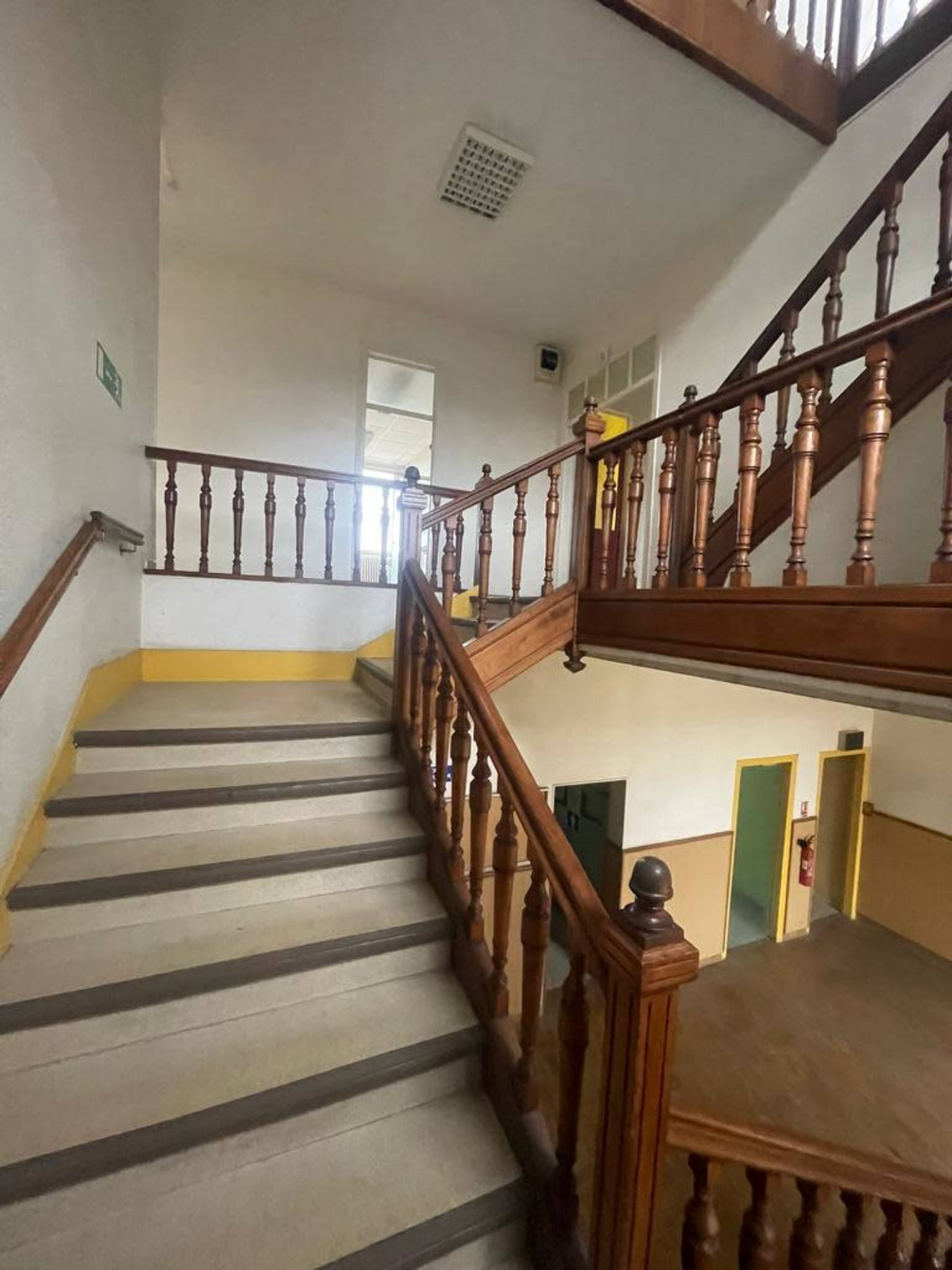 A wooden staircase with a landing leads to a second floor in a well-lit building.