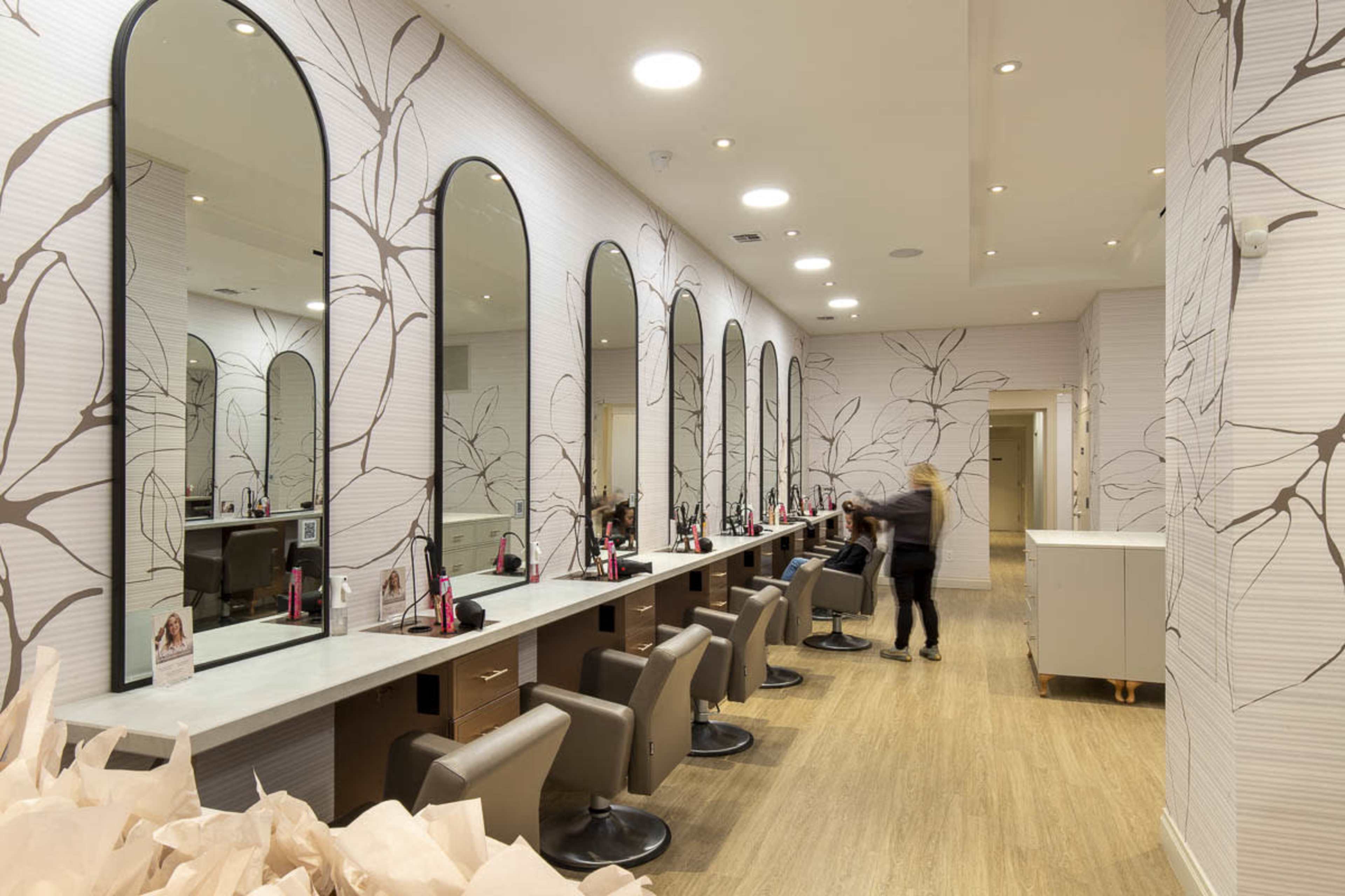 The image shows a modern hair salon with multiple styling stations featuring large mirrors and a floral-patterned wall.