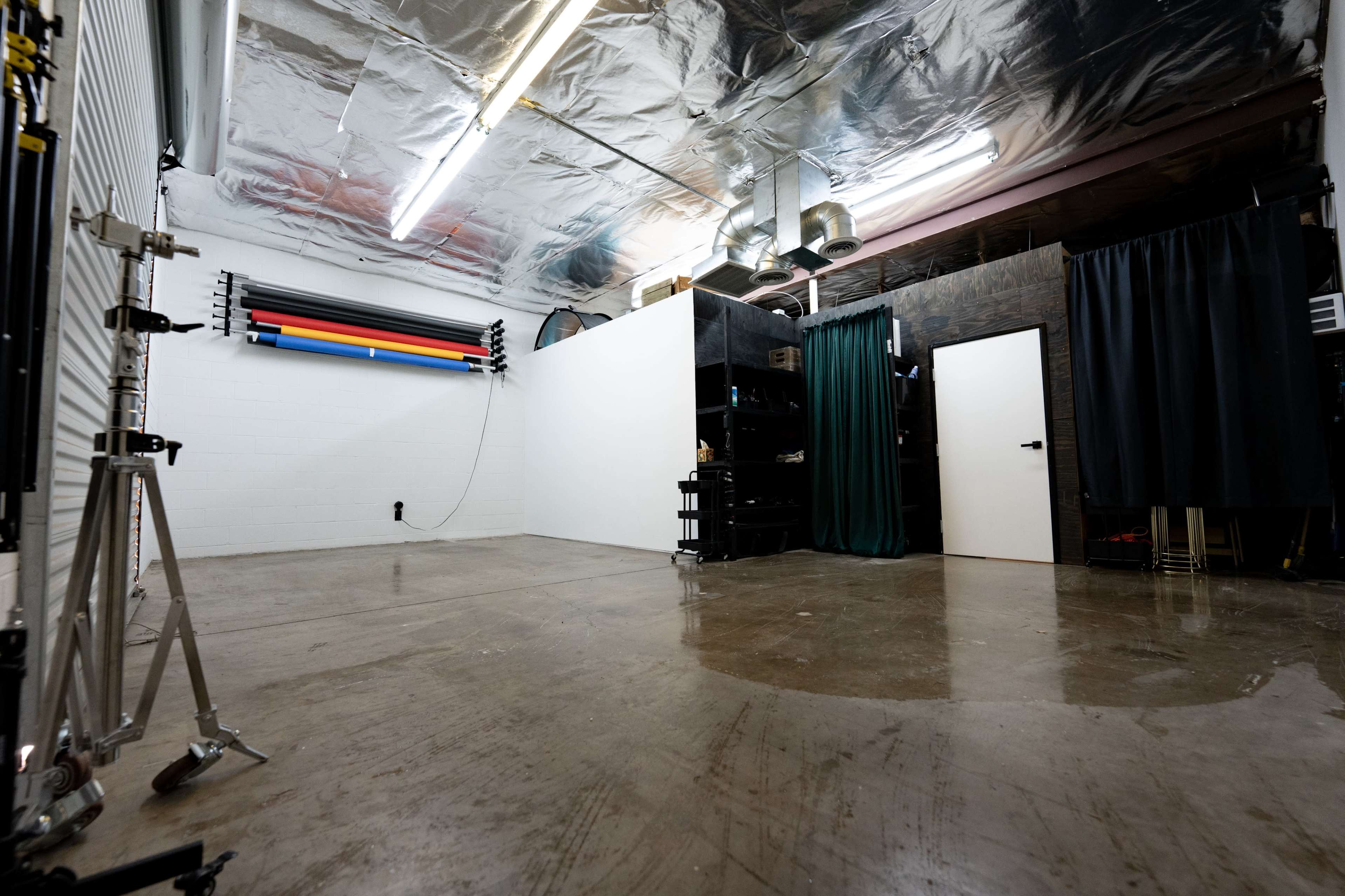 An empty studio space with concrete flooring, a ceiling covered in reflective material, and backdrop rolls hanging against a wall.
