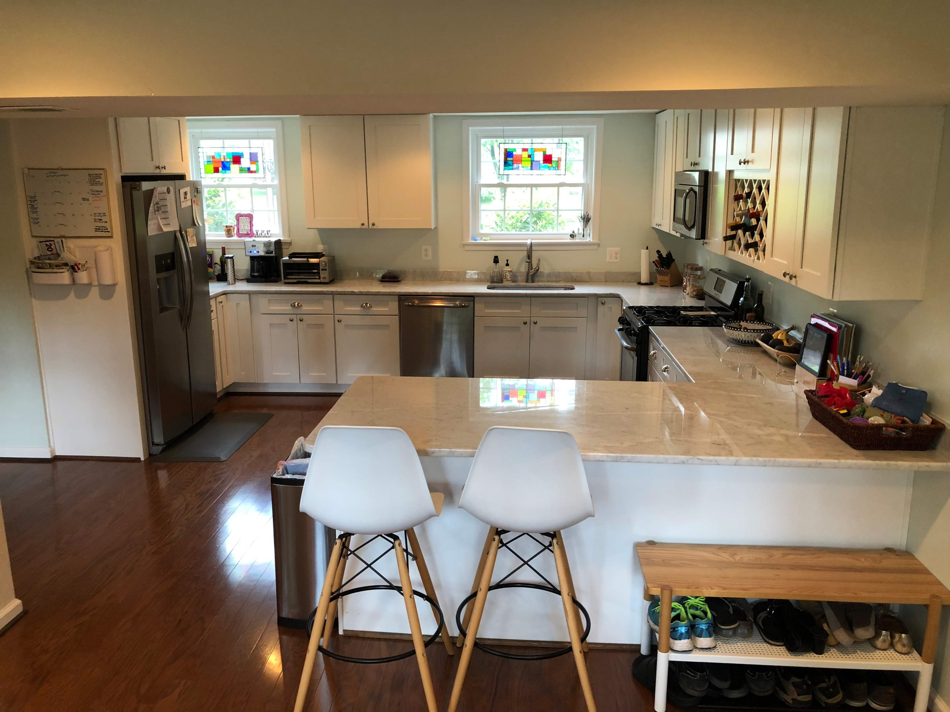 A modern kitchen featuring white cabinetry, stainless steel appliances, and a marble countertop with two bar stools.