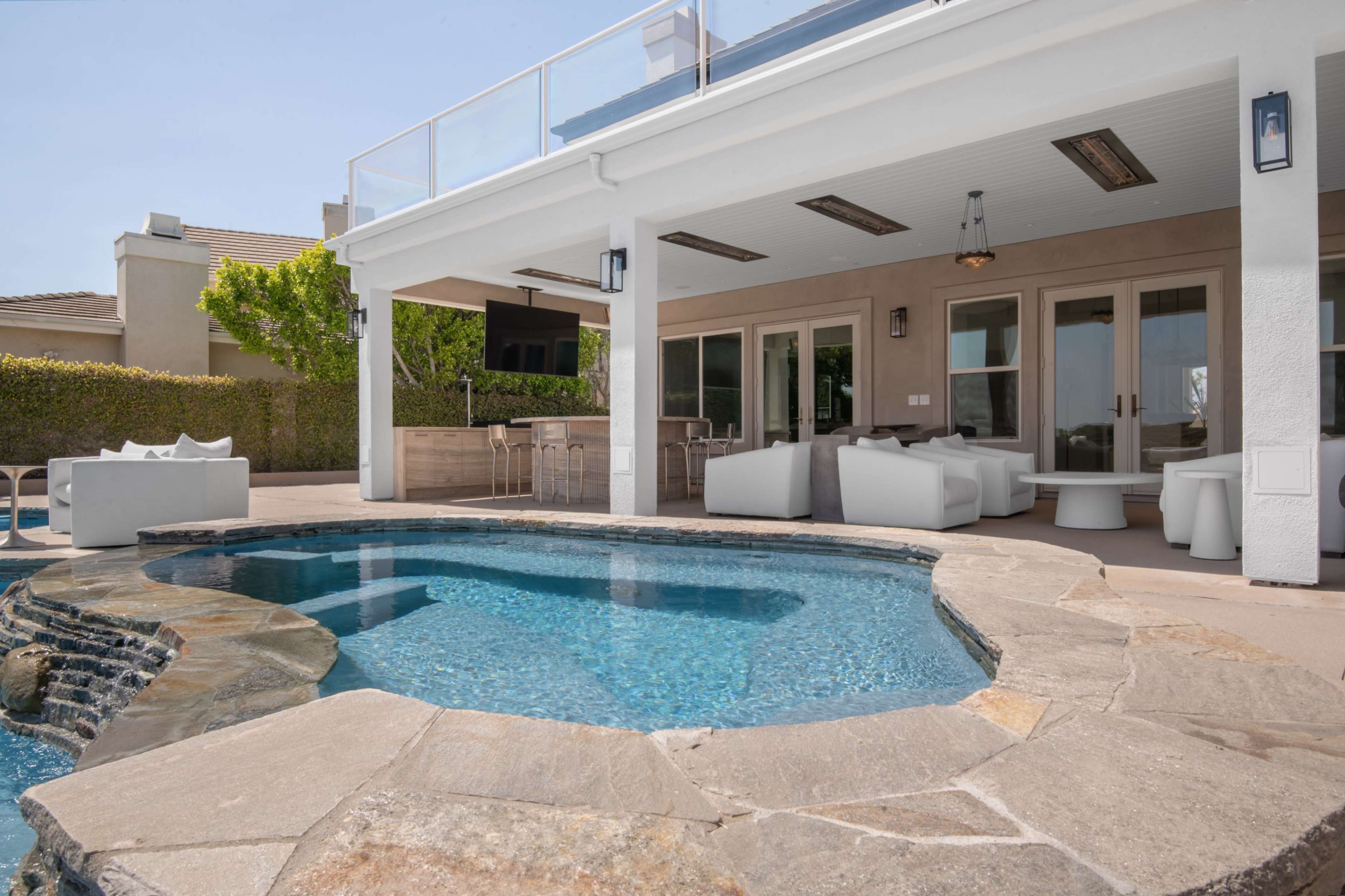 The image shows a modern outdoor area featuring a pool, a lounge space with white furniture, and a covered patio.