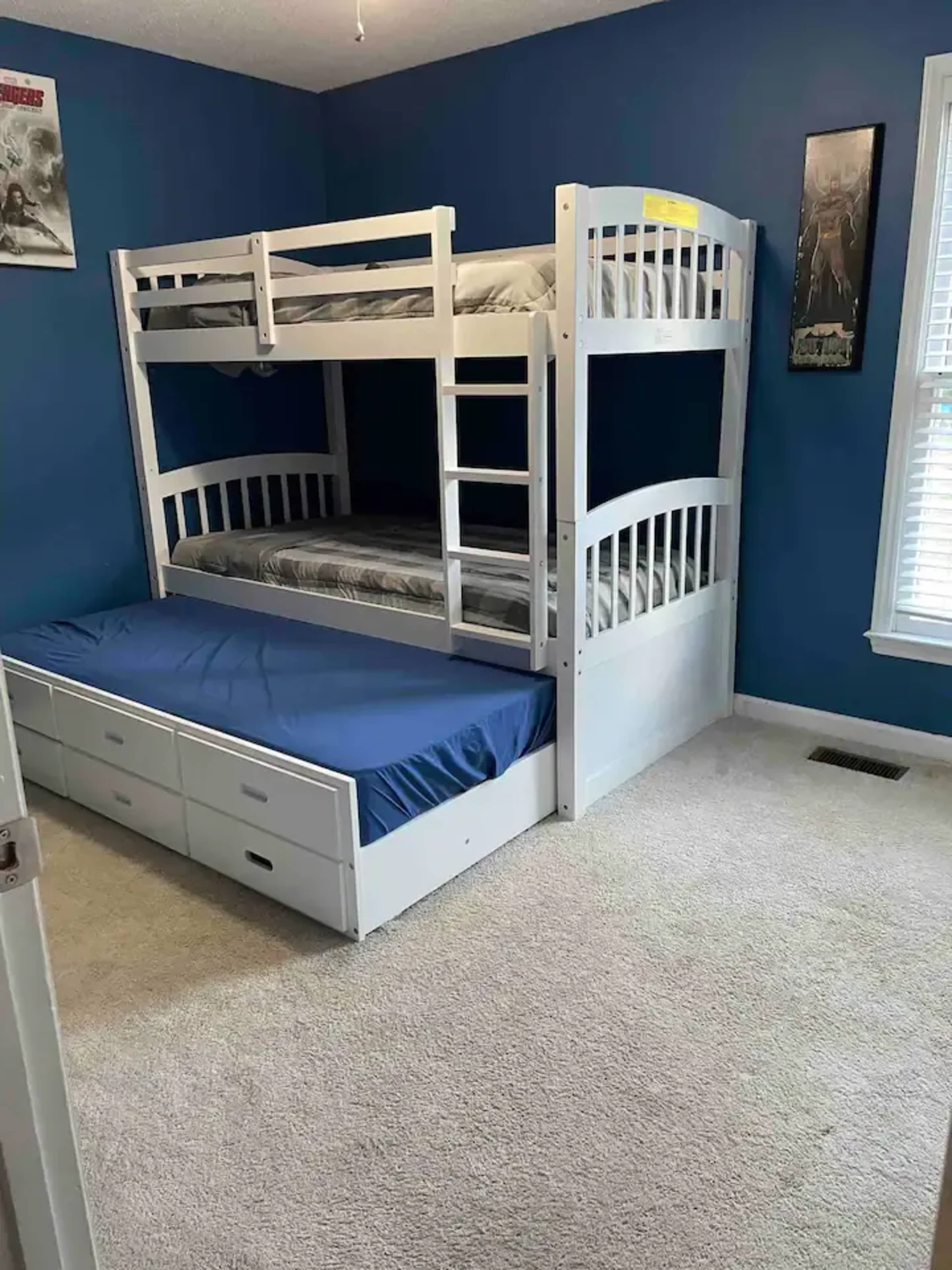 A blue-walled bedroom featuring a white bunk bed with a lower trundle bed and a carpeted floor.