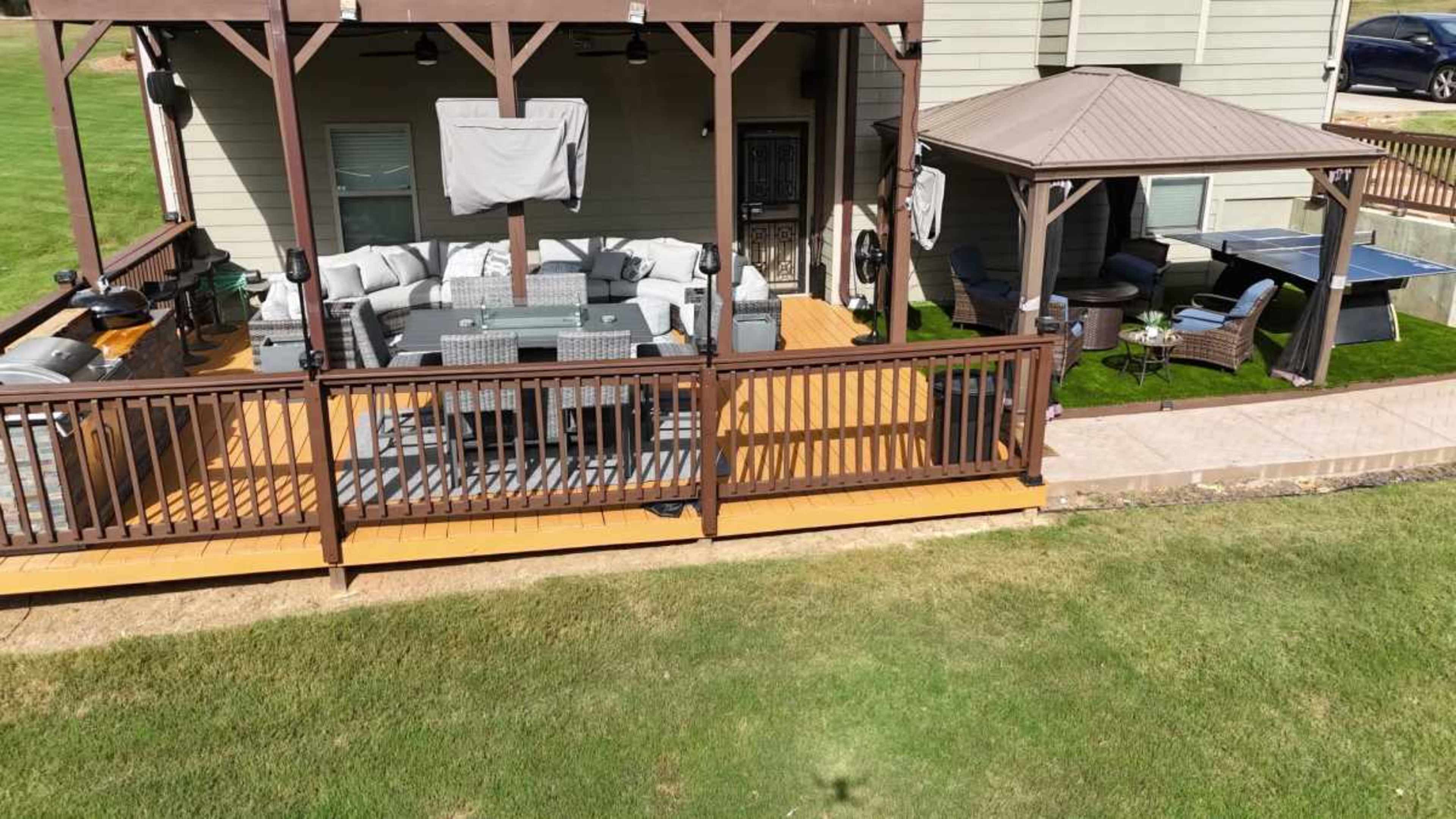 A wooden deck features a well-furnished seating area and a gazebo, surrounded by a grassy lawn.