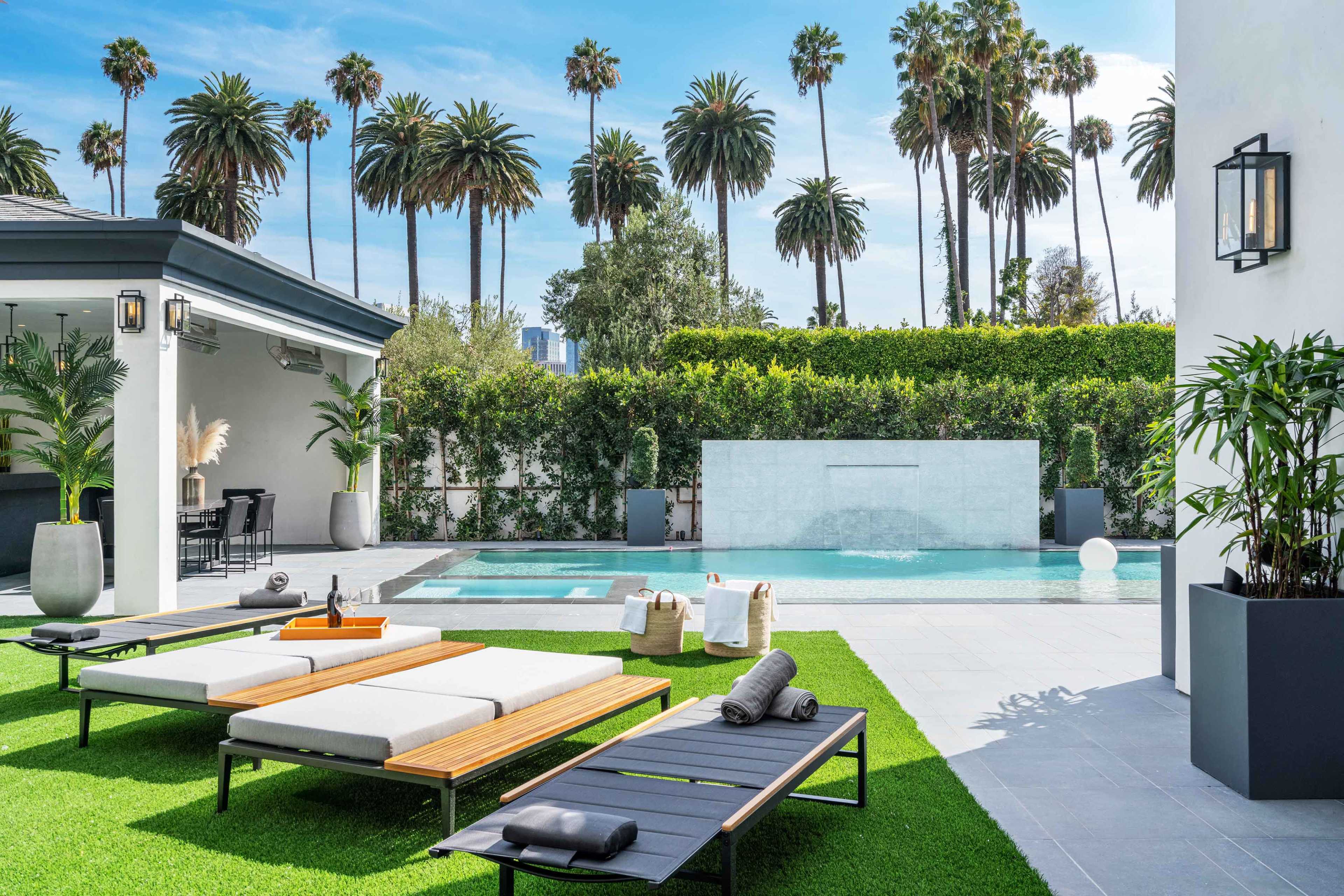 The scene features a modern outdoor space with lounge chairs, a swimming pool, and lush palm trees in the background.