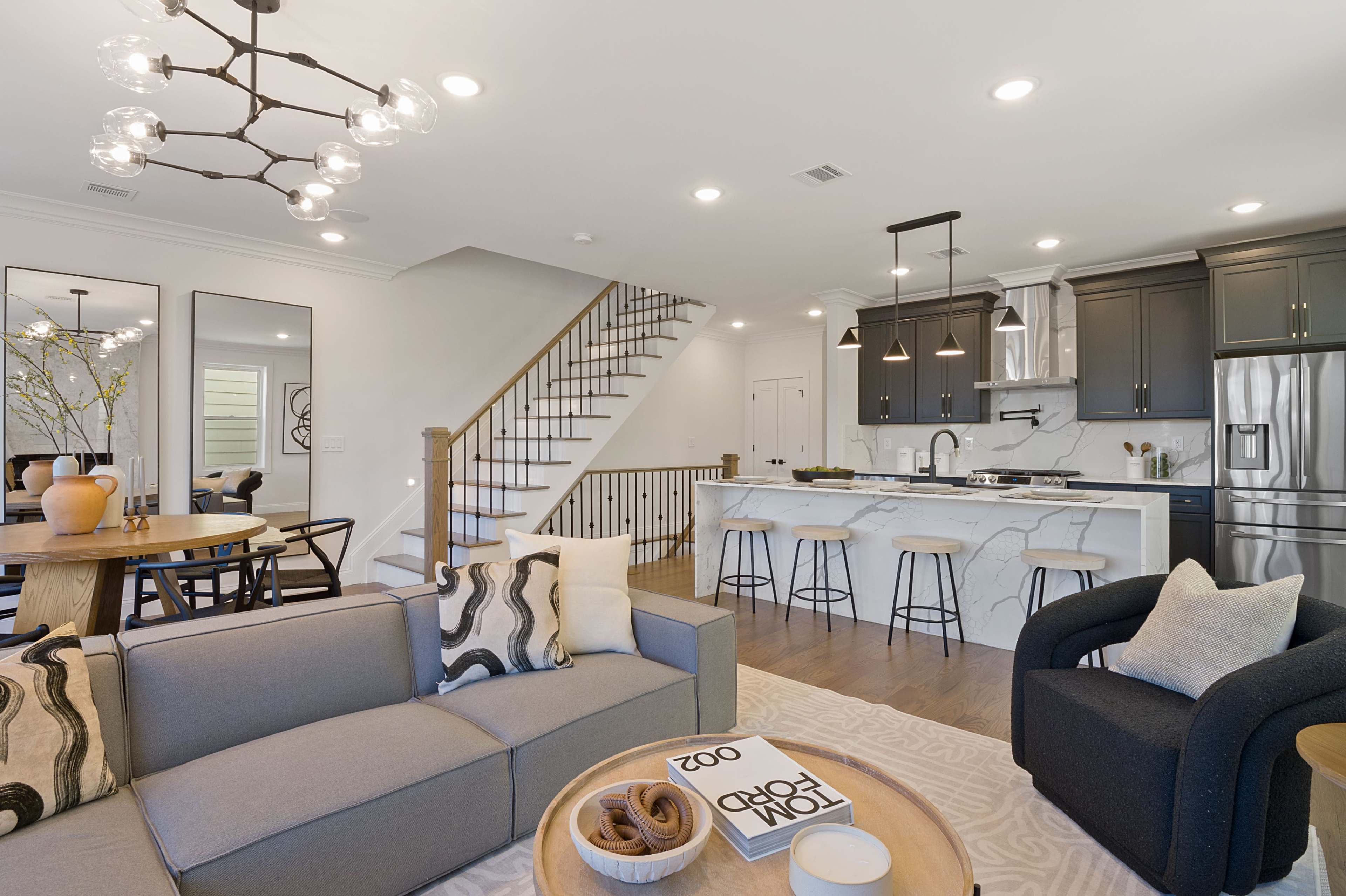 A modern open-concept living area featuring a gray sofa, a round dining table, and a kitchen with dark cabinetry and a large island.