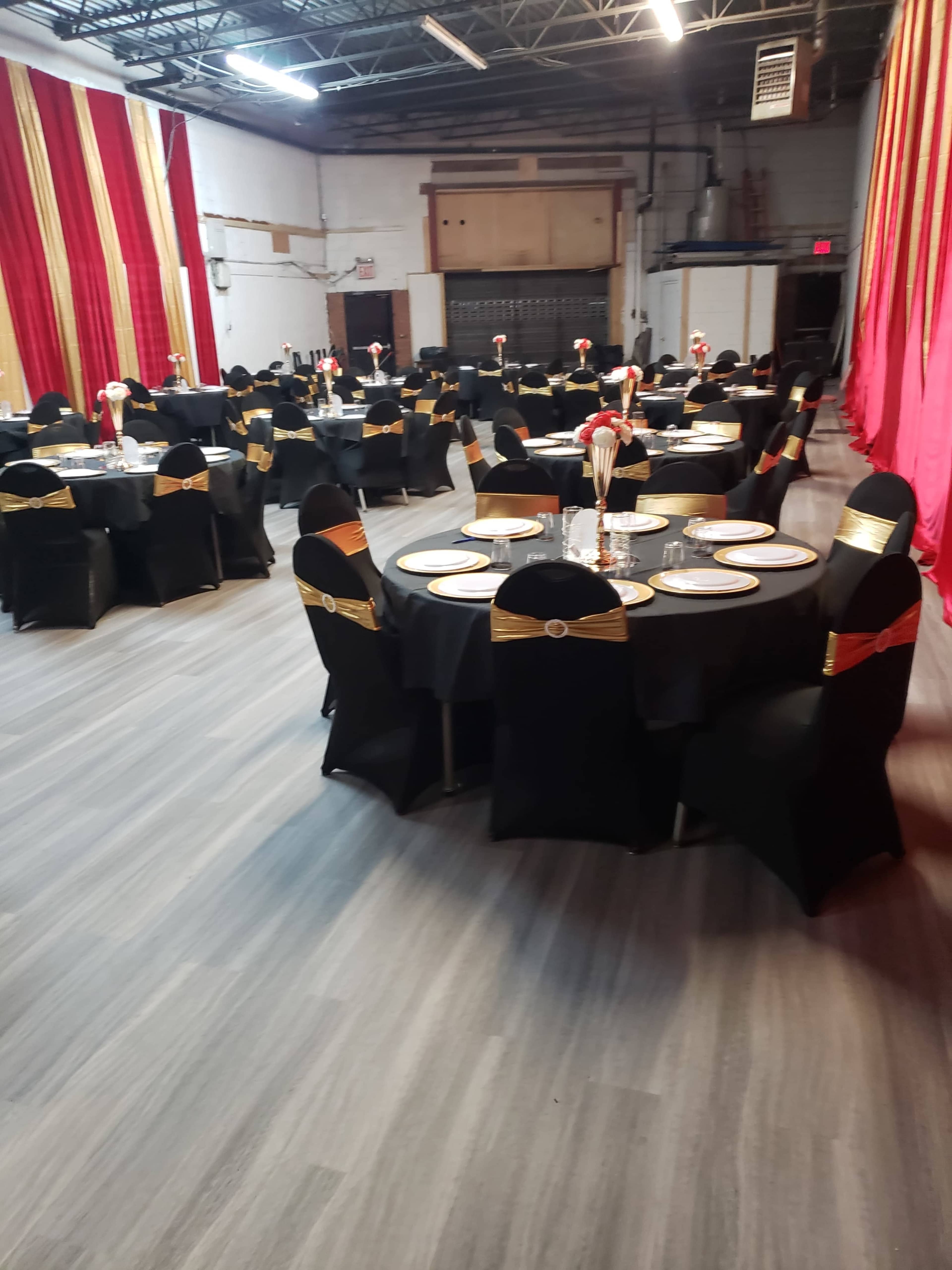 The image shows a banquet hall arranged with round tables covered in black tablecloths and gold-accented chairs, set for dining with plates and centerpieces.