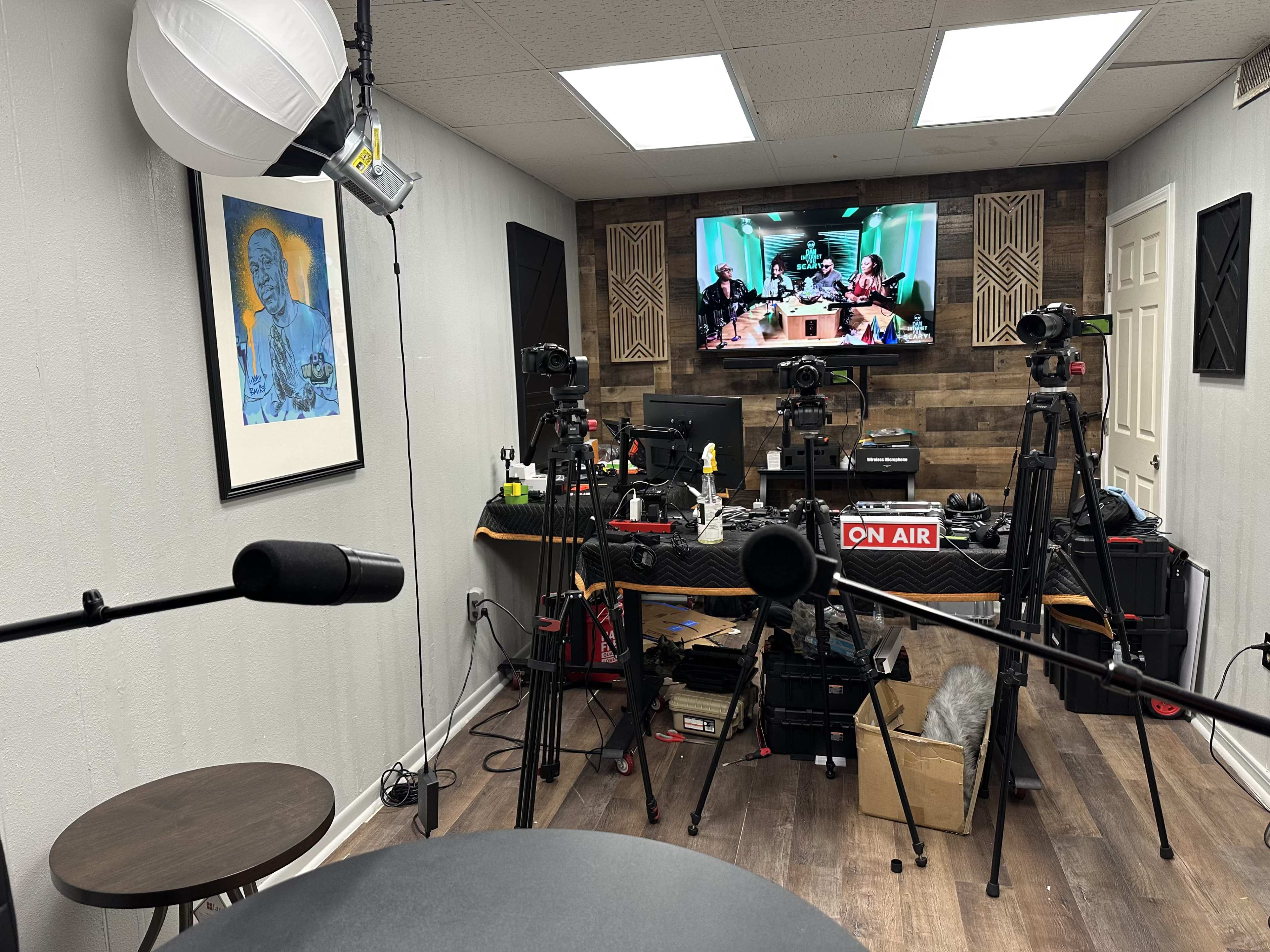 A recording studio features multiple cameras, microphones, and a large monitor displaying a group discussion.