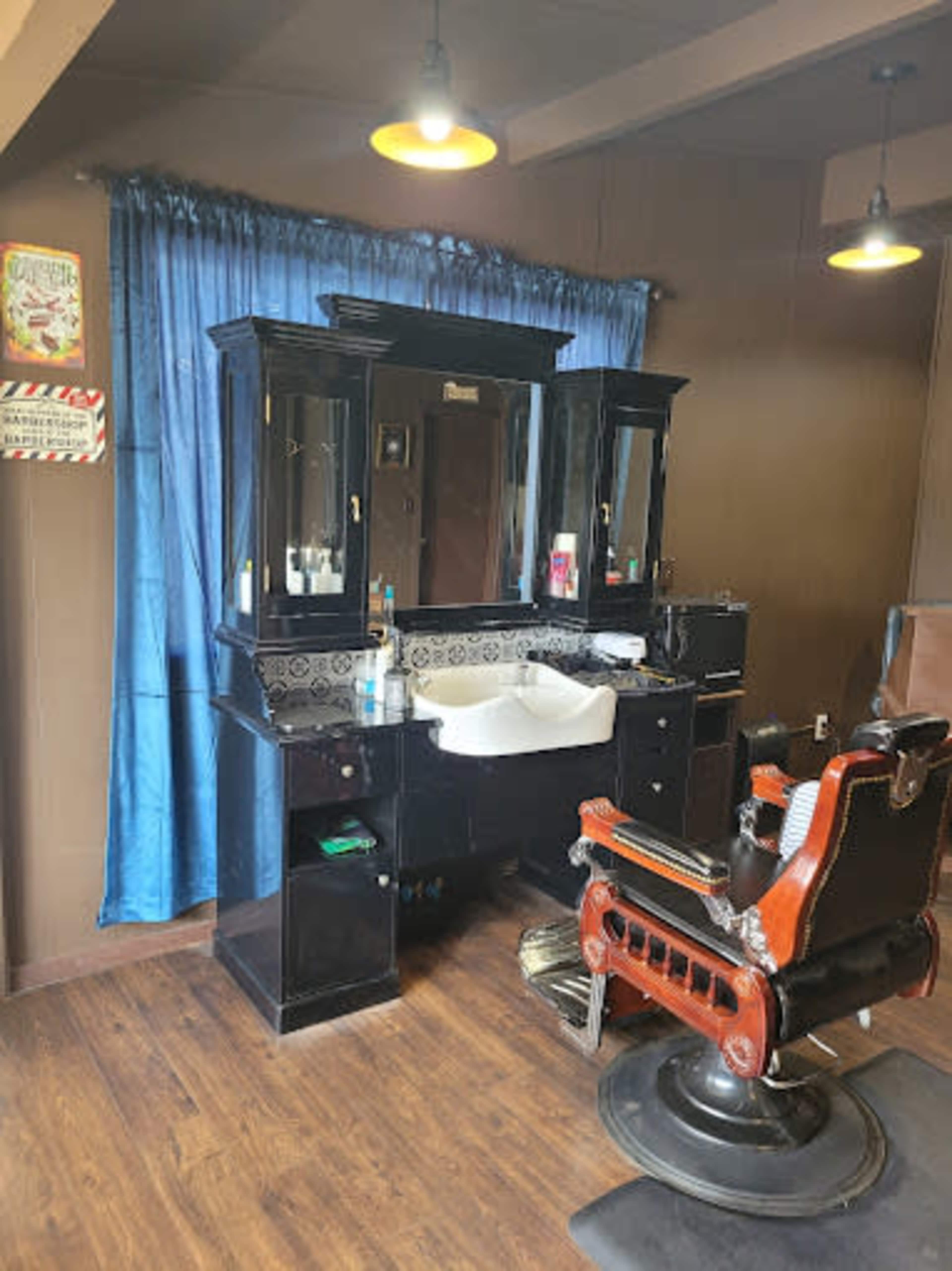 The image shows a barber shop interior featuring a vintage barber chair in front of a large mirror and a sink, with blue curtains in the background.