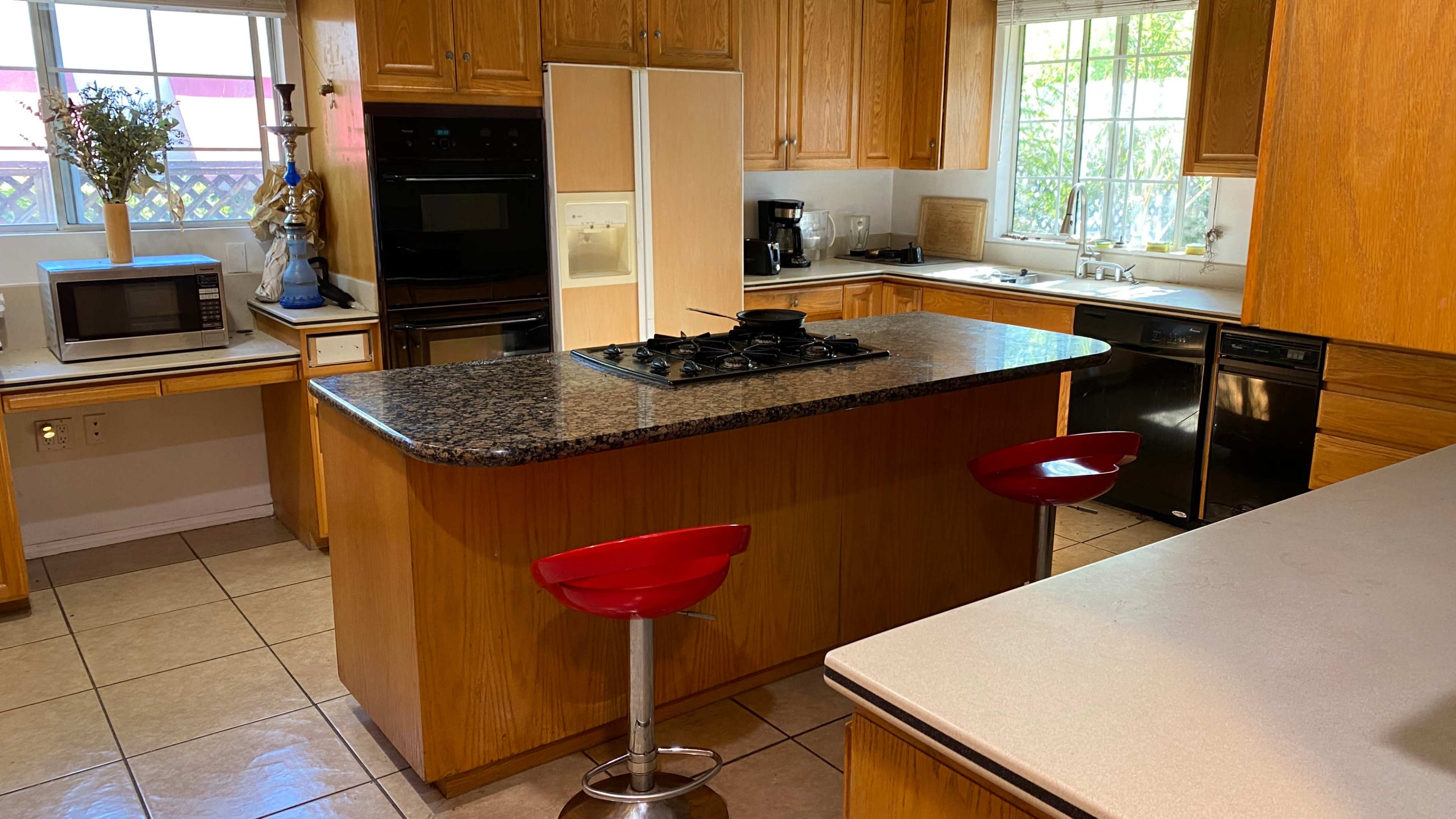 A spacious kitchen features wooden cabinets, a granite island with a black cooktop, and modern appliances, including a microwave and dishwasher.