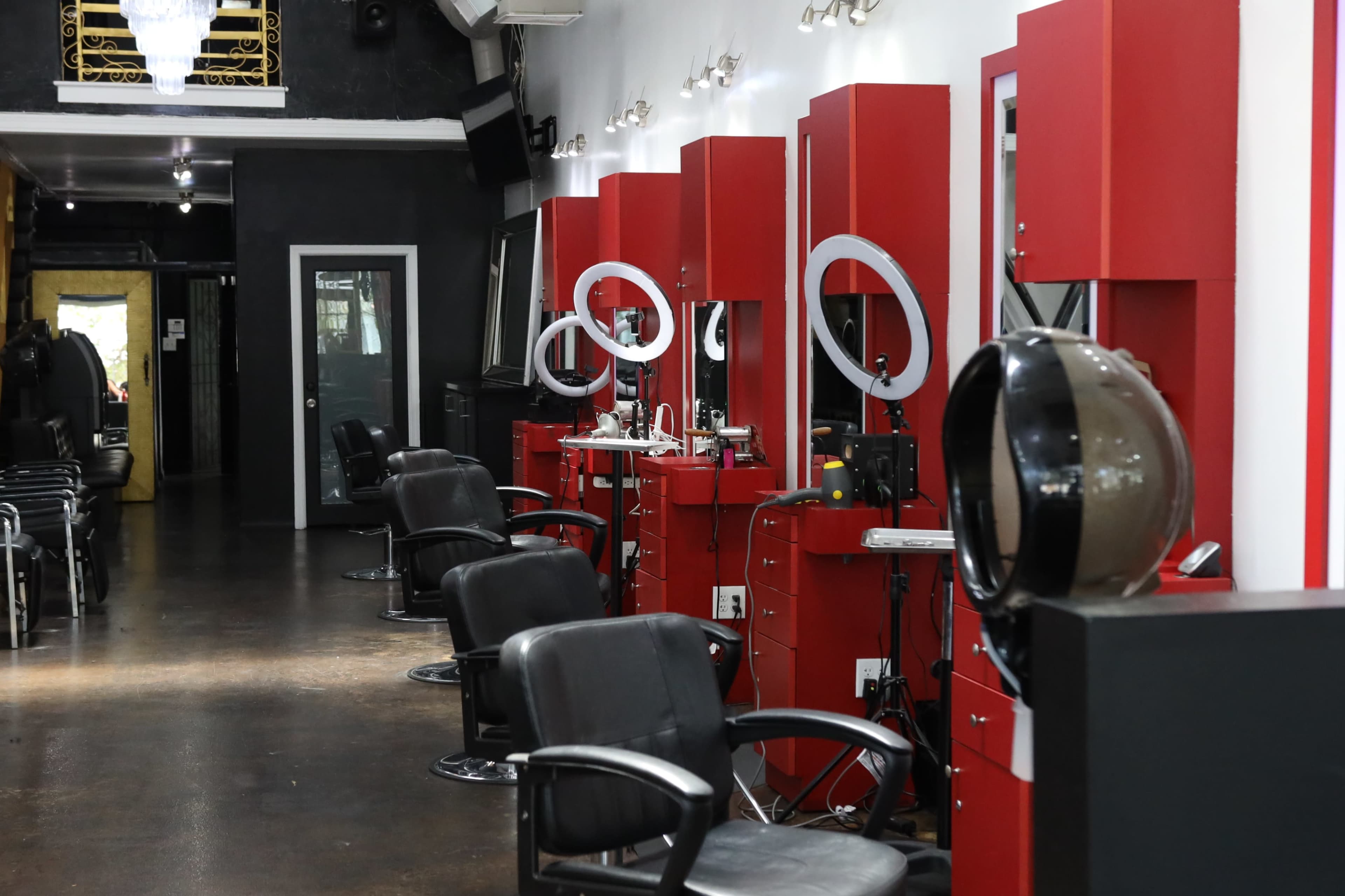 The image shows a hair salon interior featuring several red styling stations with round mirrors and black chairs, along with a waiting area visible in the background.