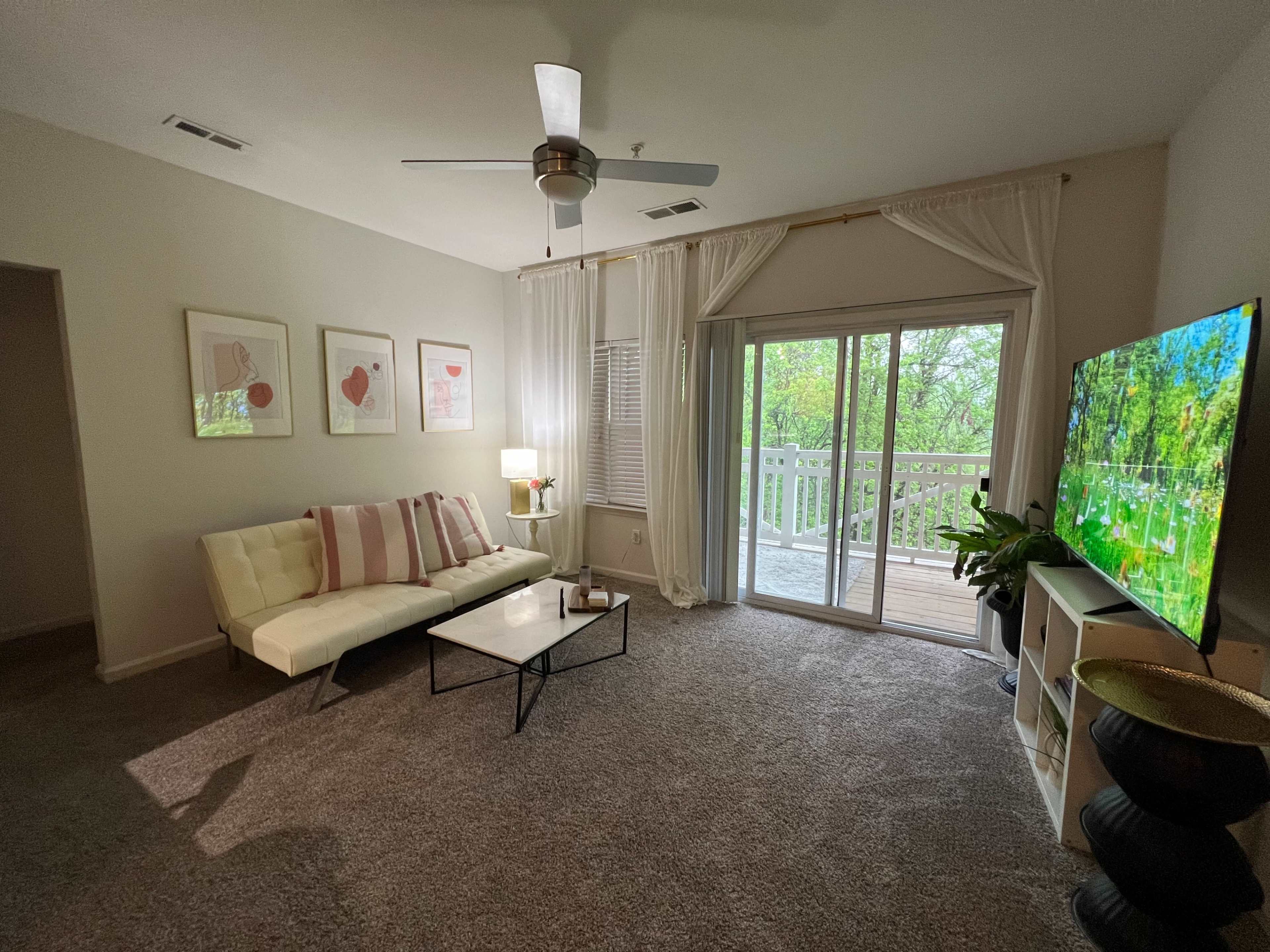 A living room features a white sofa, a black coffee table, and a large window with a sliding door leading to a balcony.