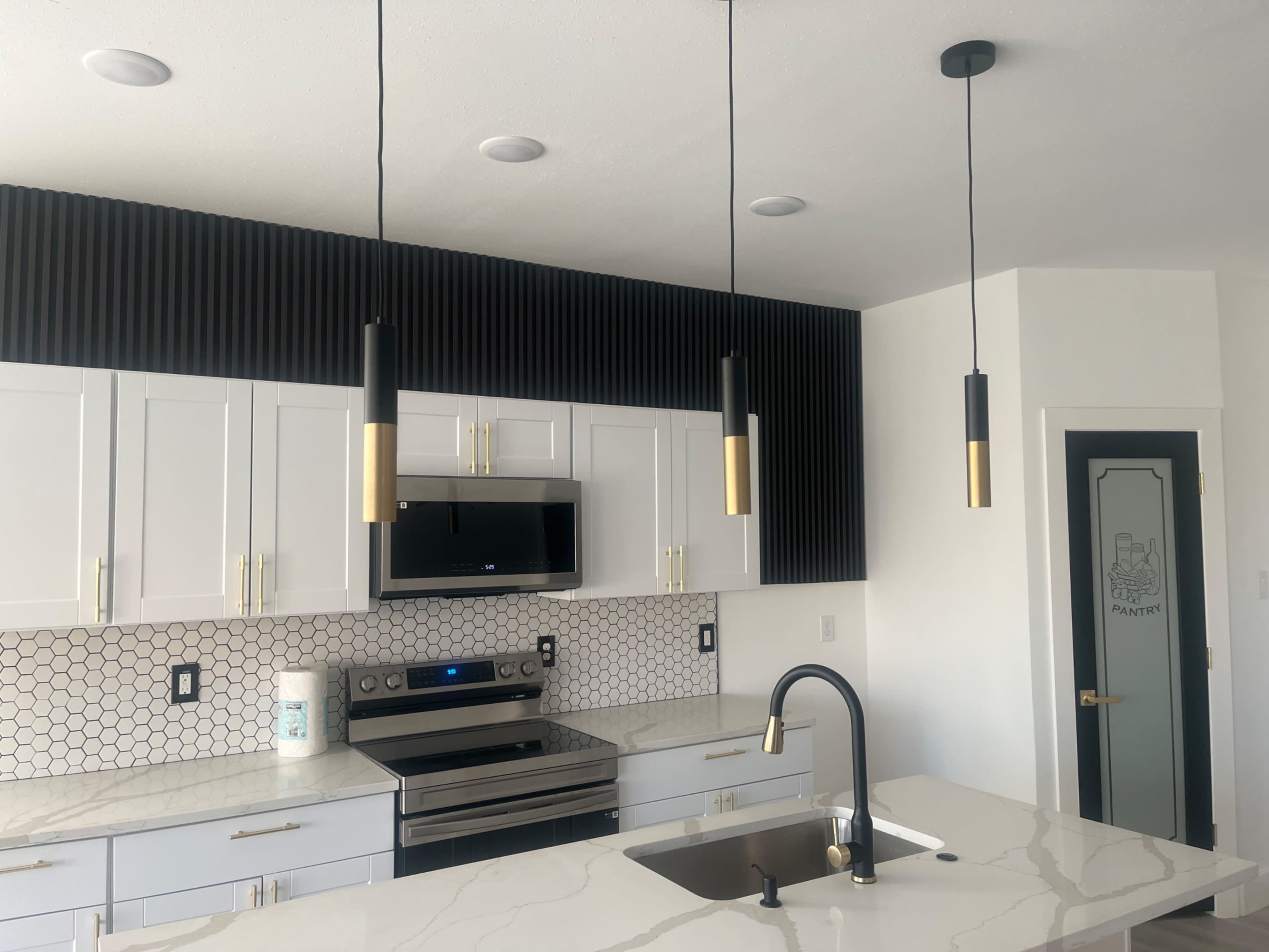 The image shows a modern kitchen featuring white cabinetry, a hexagonal tile backsplash, stainless steel appliances, and three hanging pendant lights over a central island.