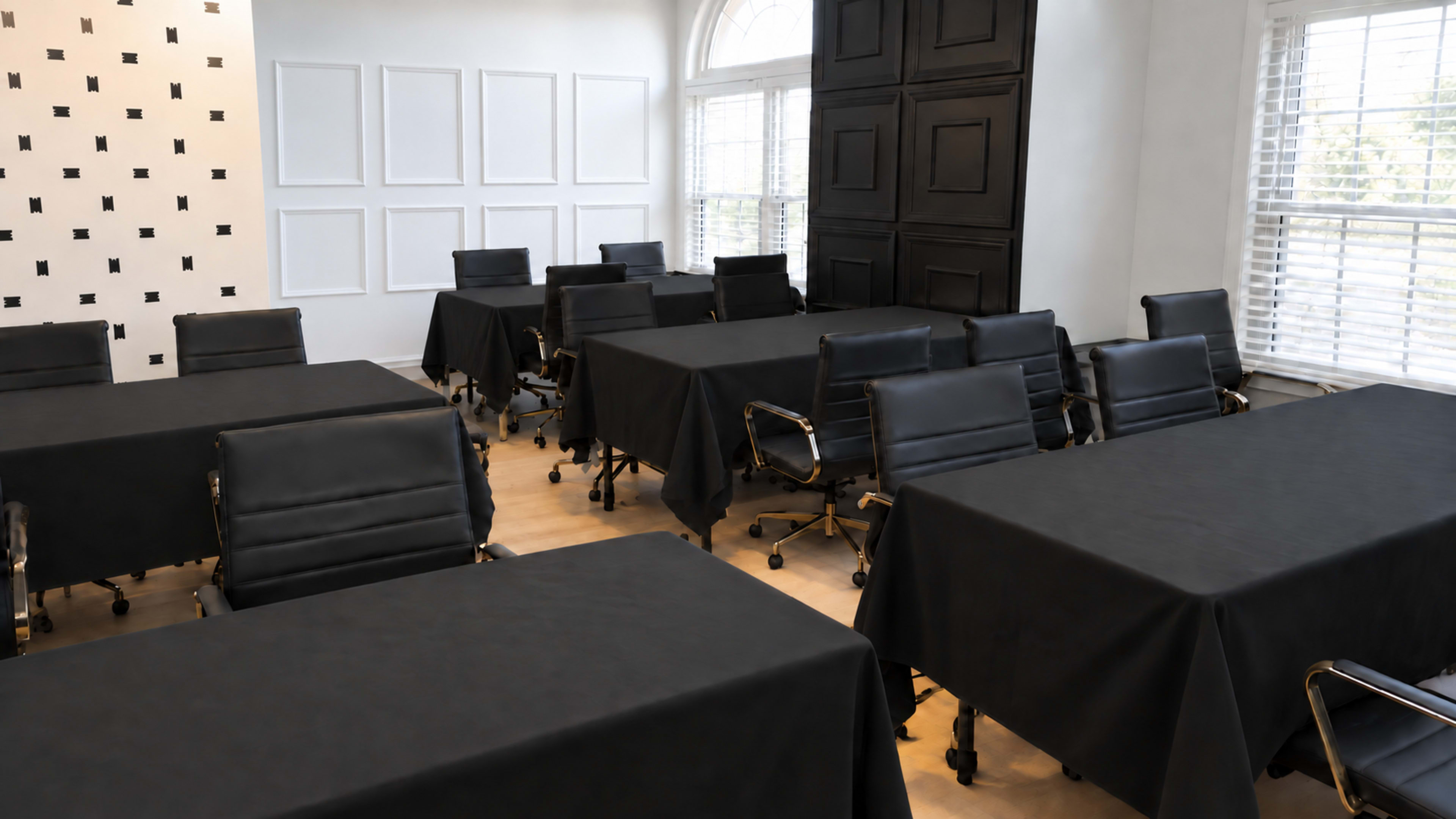 The image shows a conference room set up with multiple black tables and chairs arranged for a meeting.