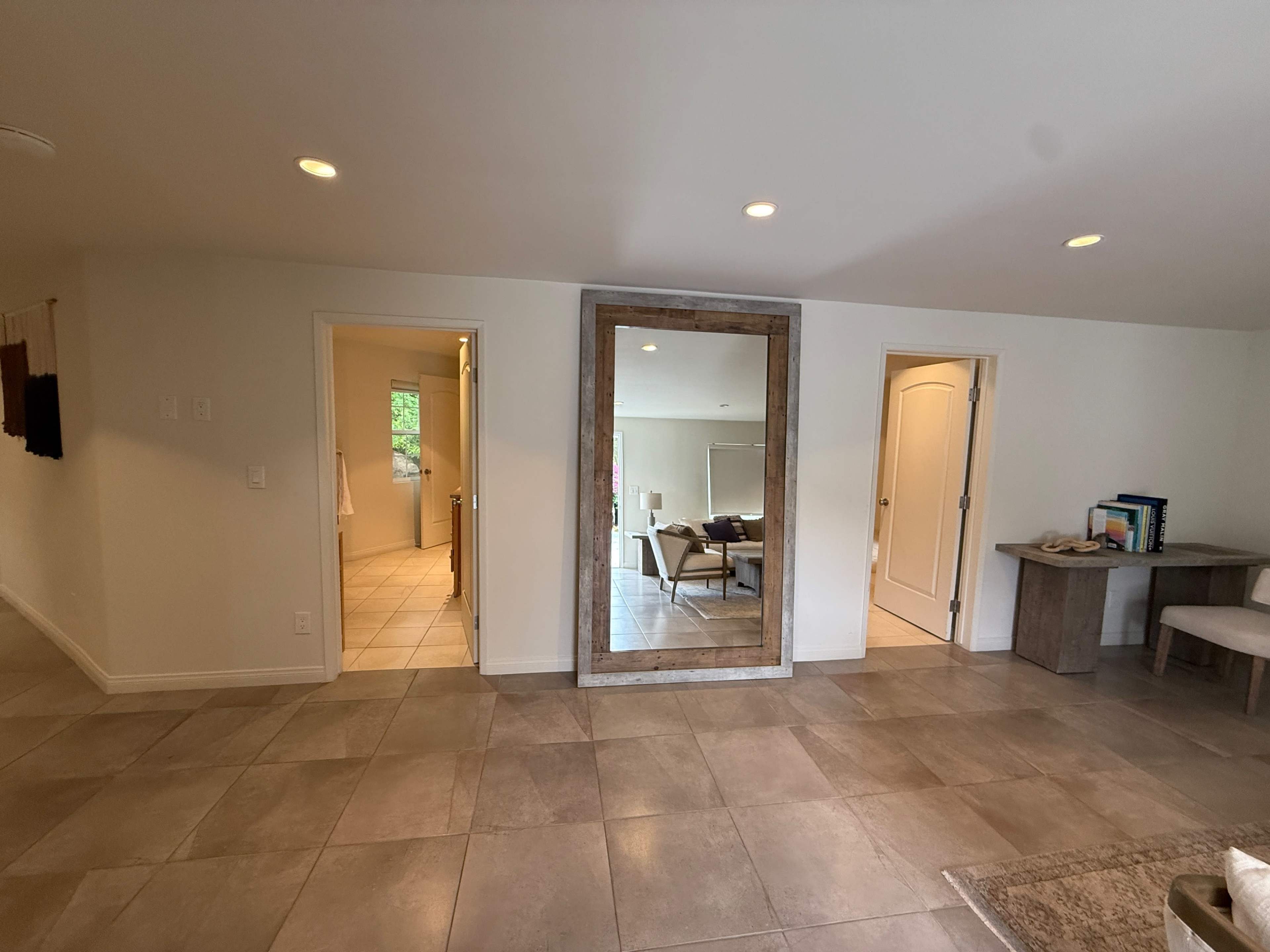 The image shows a spacious interior area featuring a large mirror framed in wood, with two doorways leading to separate rooms on either side.