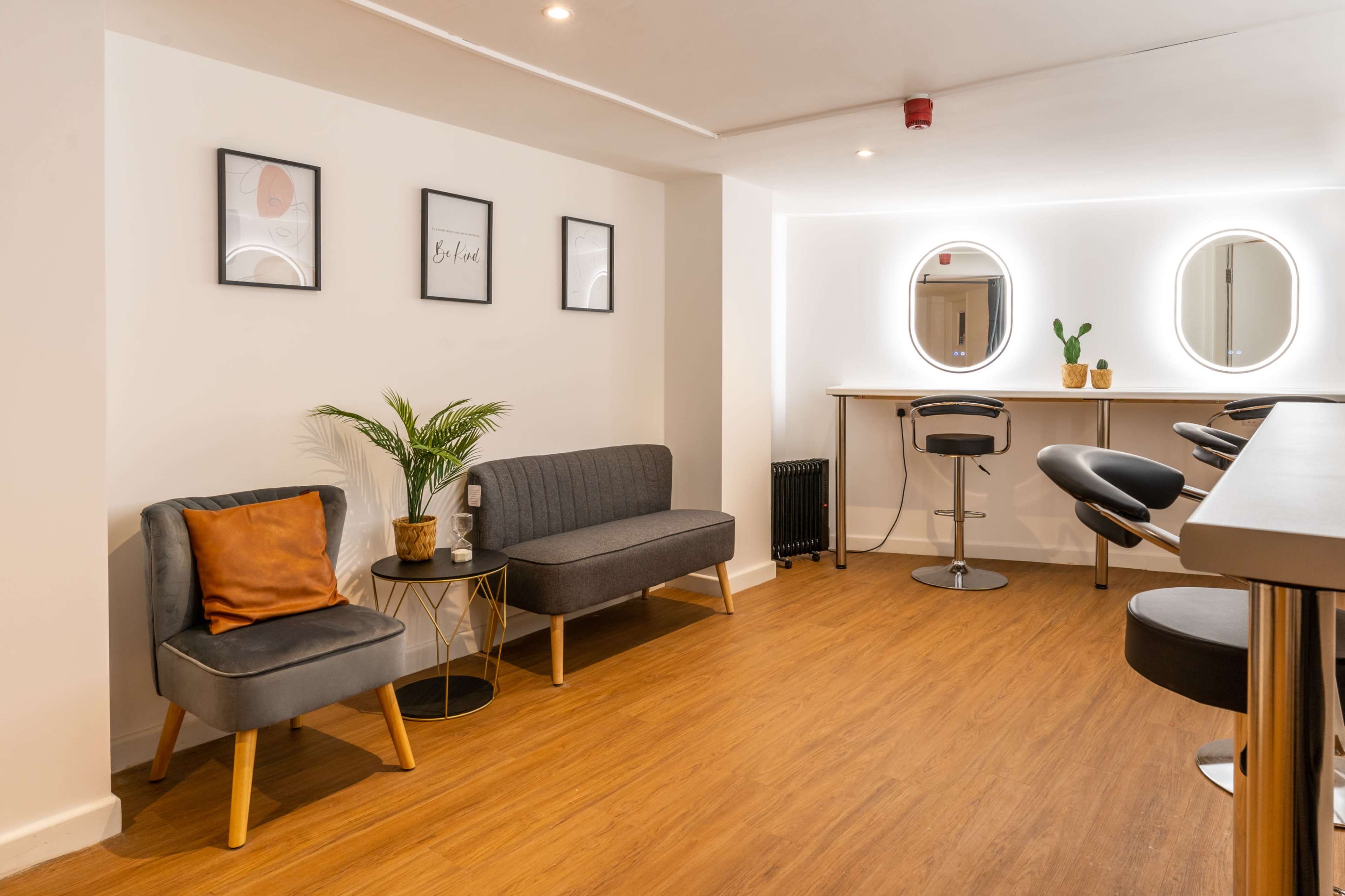 A modern waiting area with two chairs, a circular mirror above a bar-style counter, and a small potted plant.