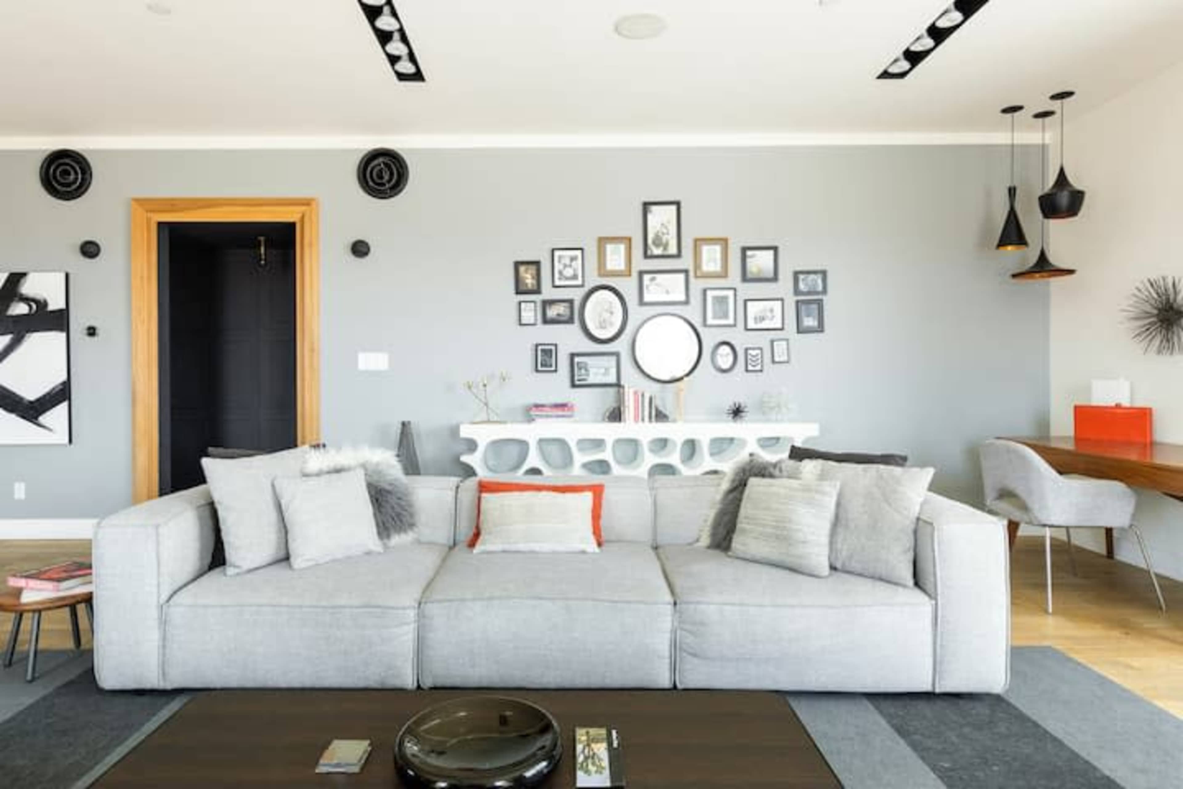 A modern living room featuring a gray sectional sofa, a gallery wall of framed artwork, and a sleek table with decorative elements.
