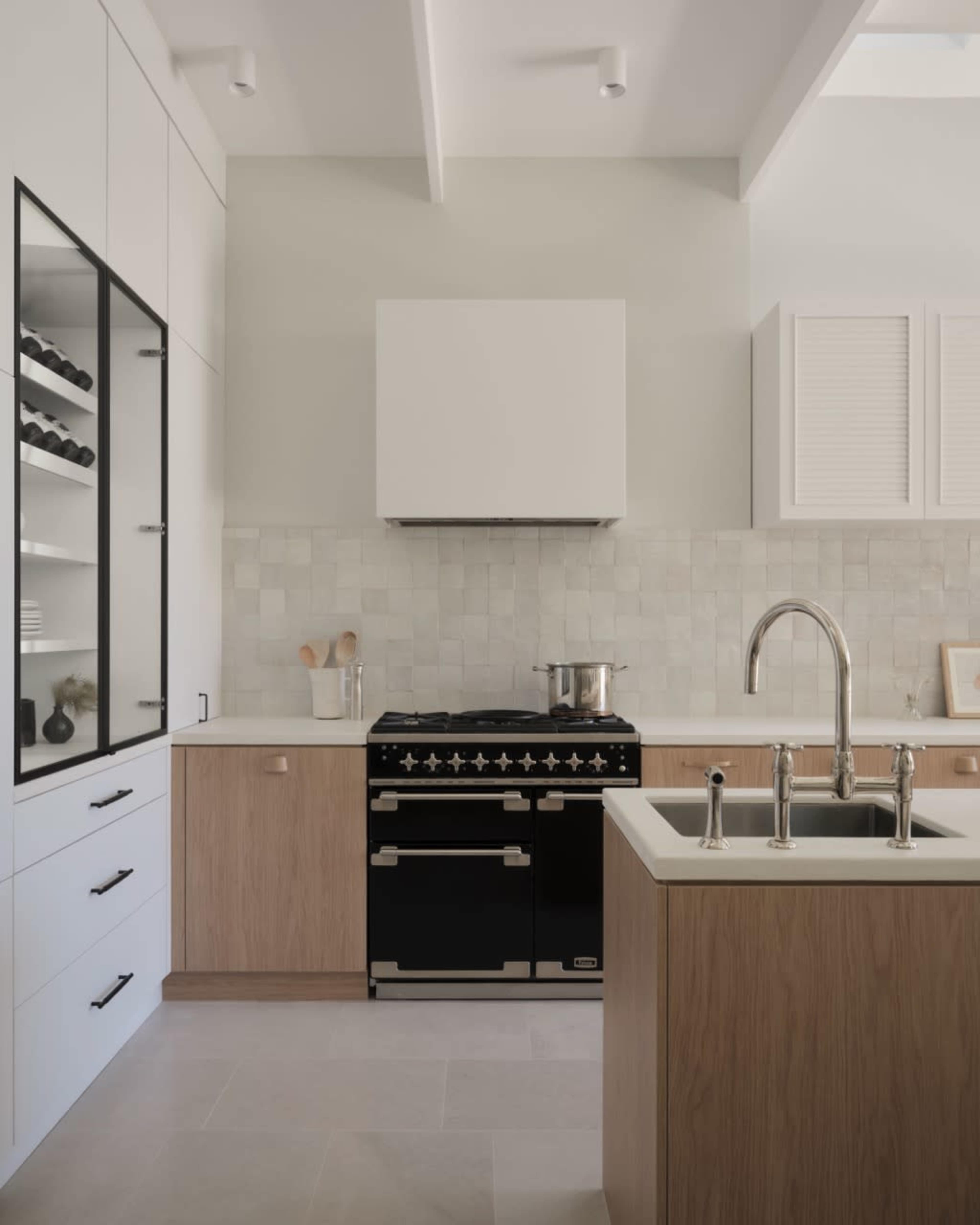 The kitchen features a mix of light wood cabinetry and white panels, with a black gas range and a stainless steel faucet.