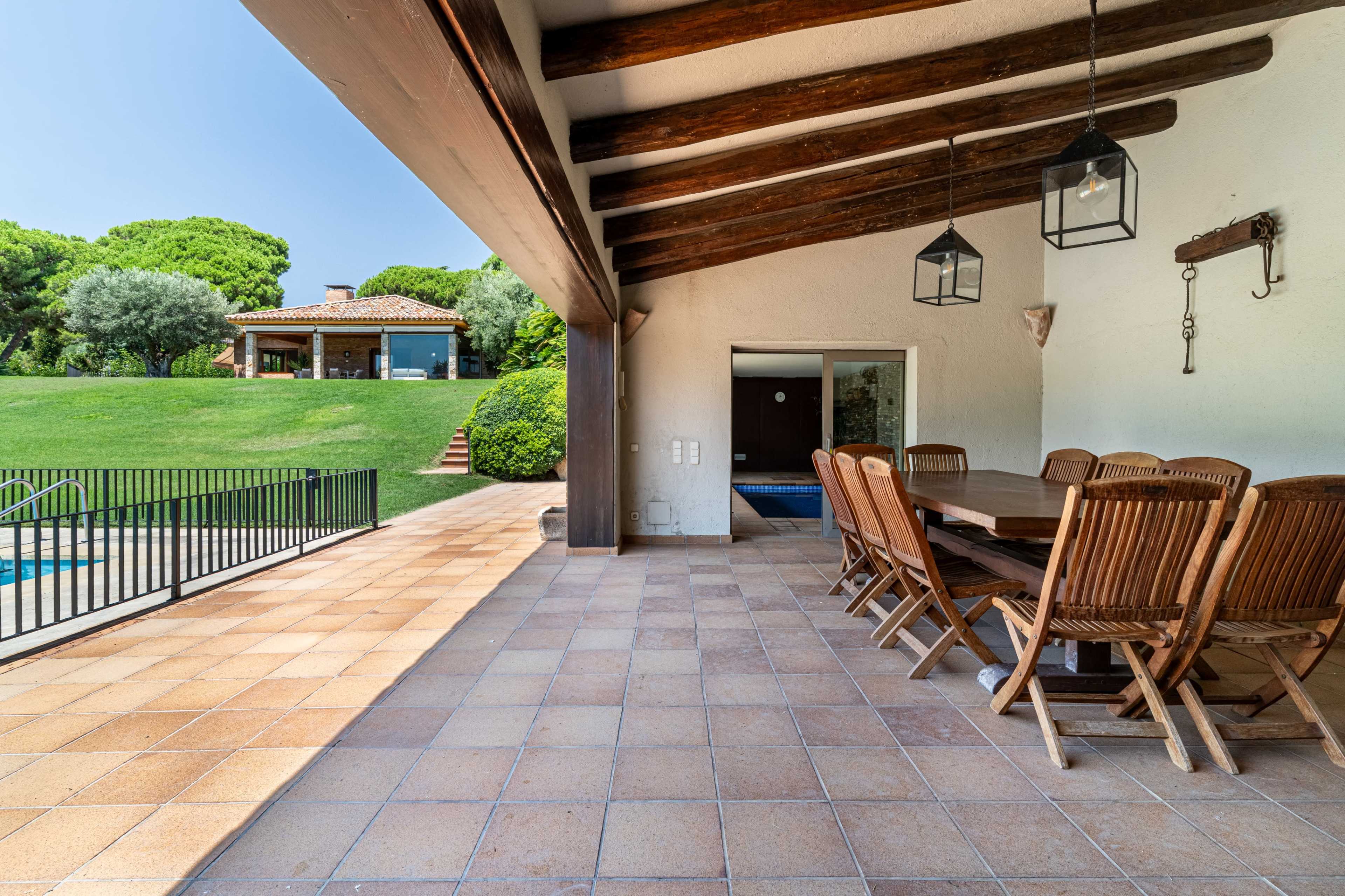 A spacious outdoor dining area features a wooden table and chairs, overlooking a green lawn and a house with large glass doors.