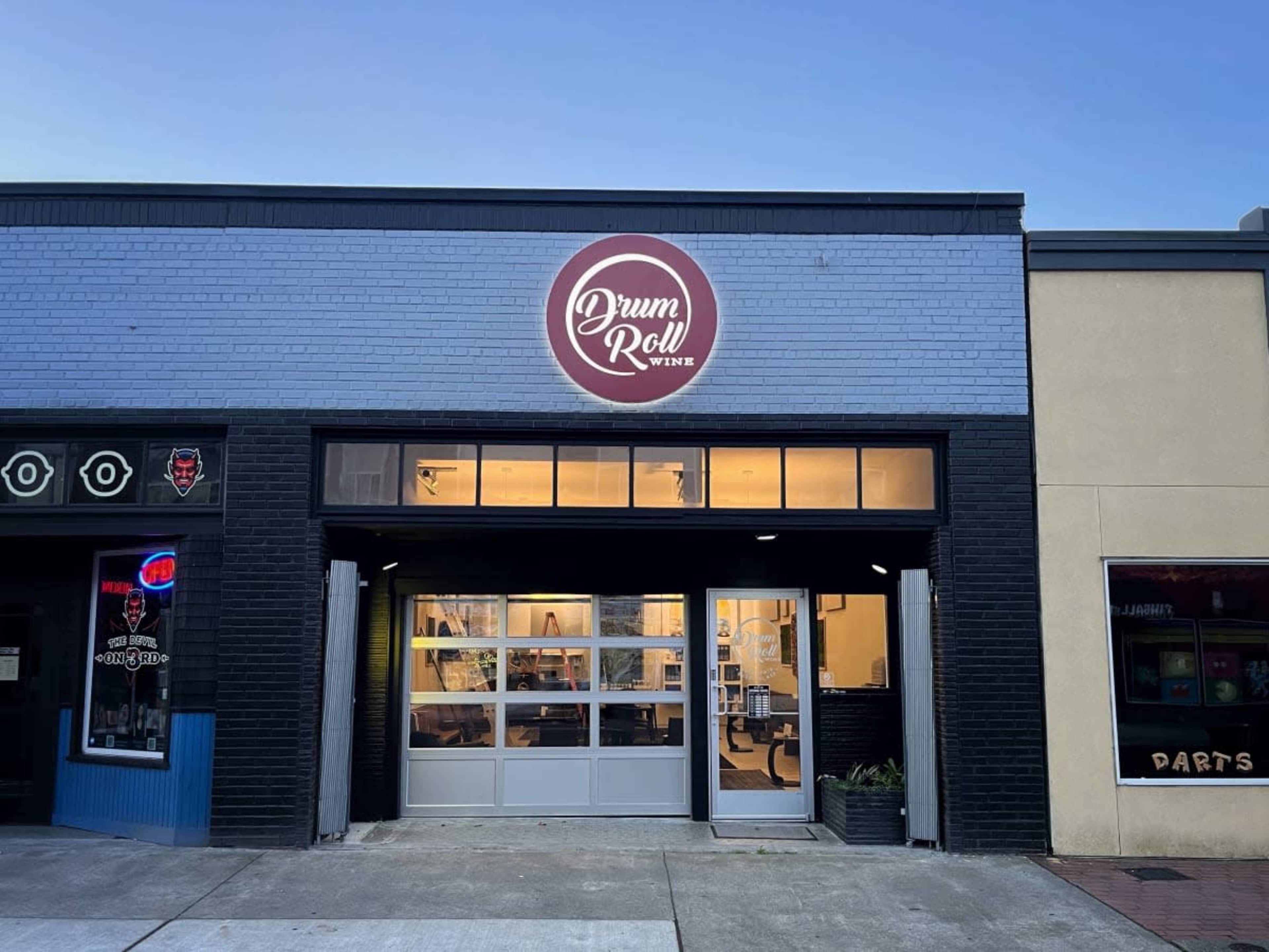 A storefront with a sign that reads "Drum Roll Wine," featuring large windows and a sleek entrance.