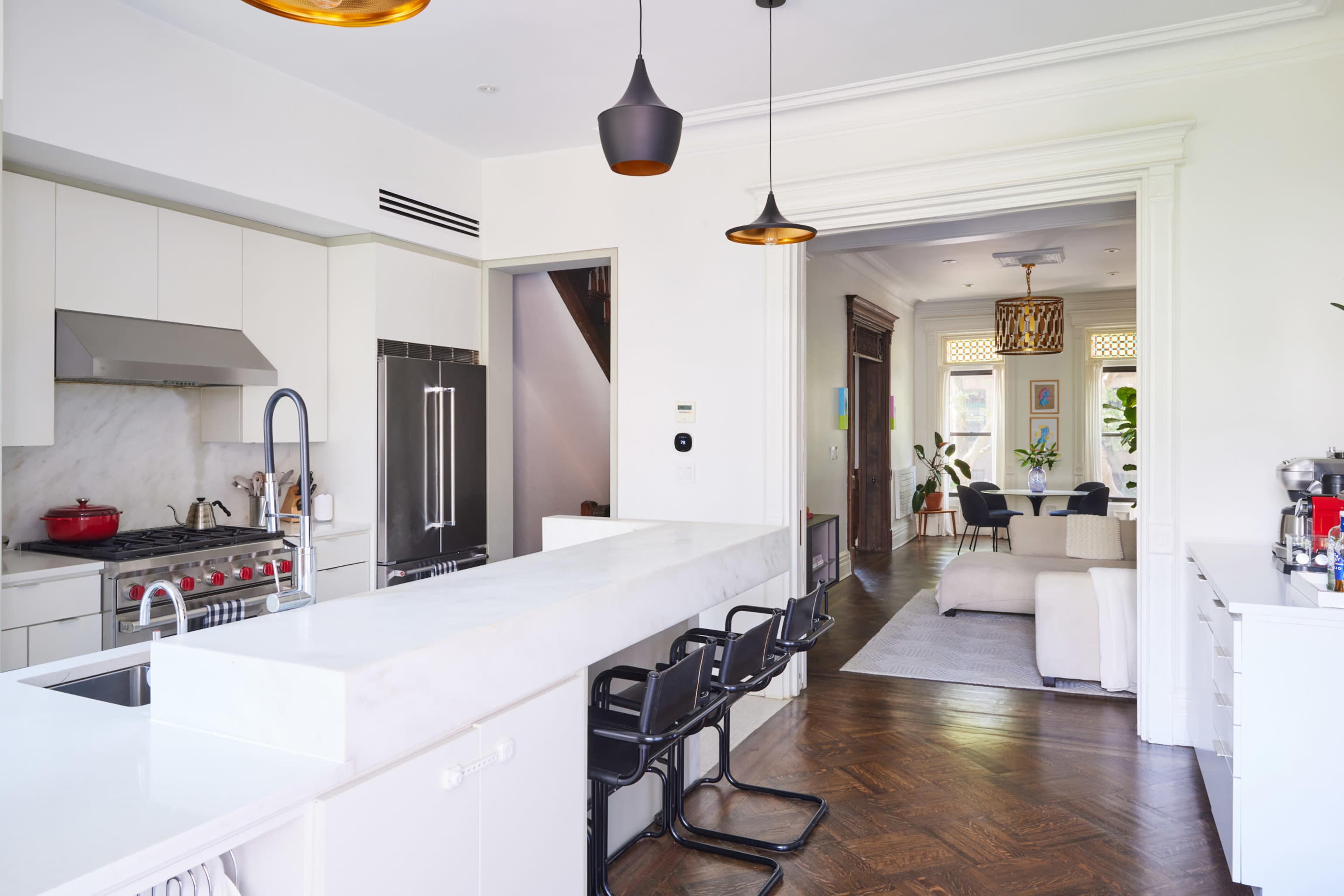 A modern kitchen with a marble countertop, black bar stools, and an open layout leading into a living area.