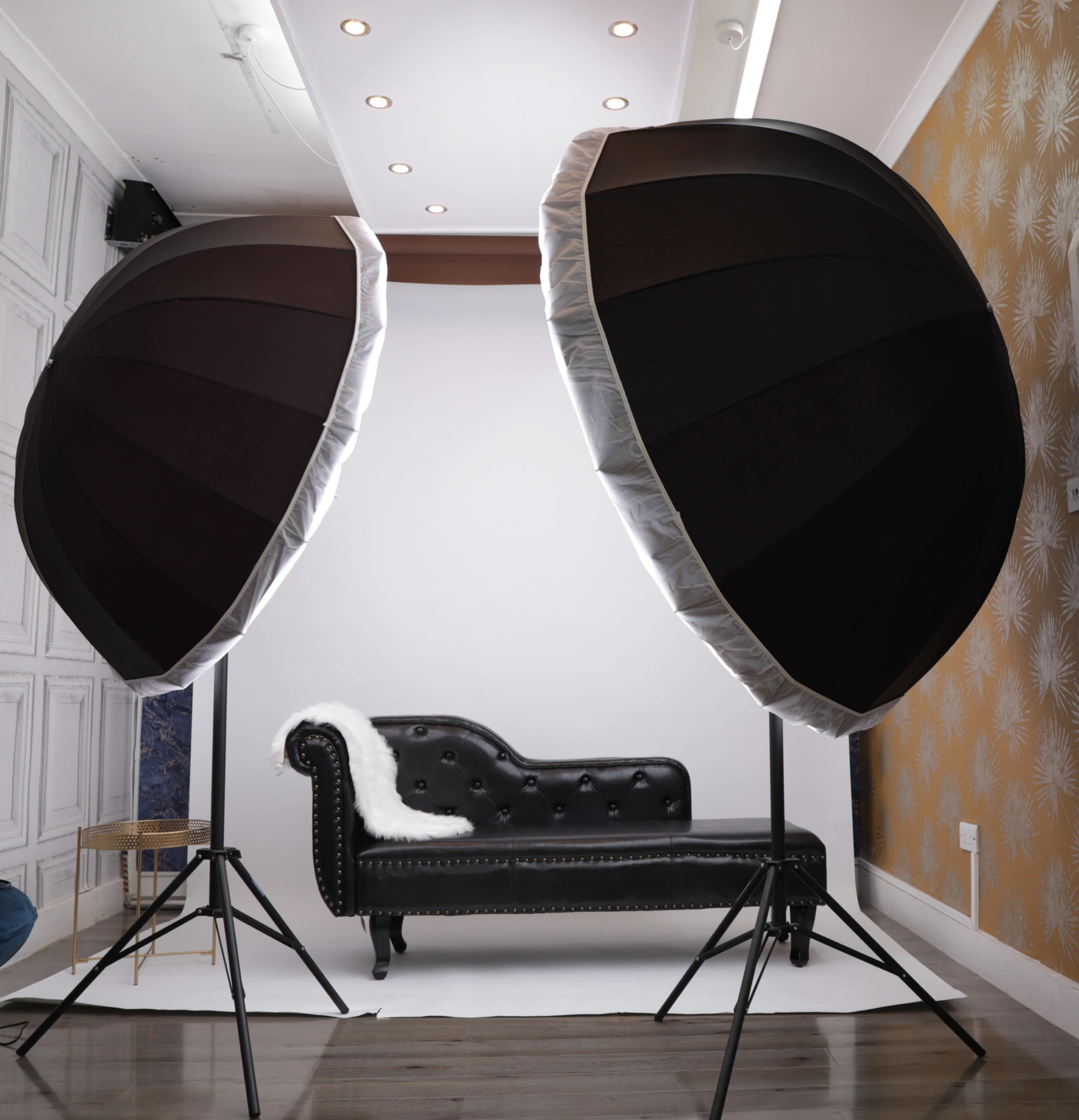 A photography studio setup with two large softbox lights flanking a black tufted sofa against a blank backdrop.