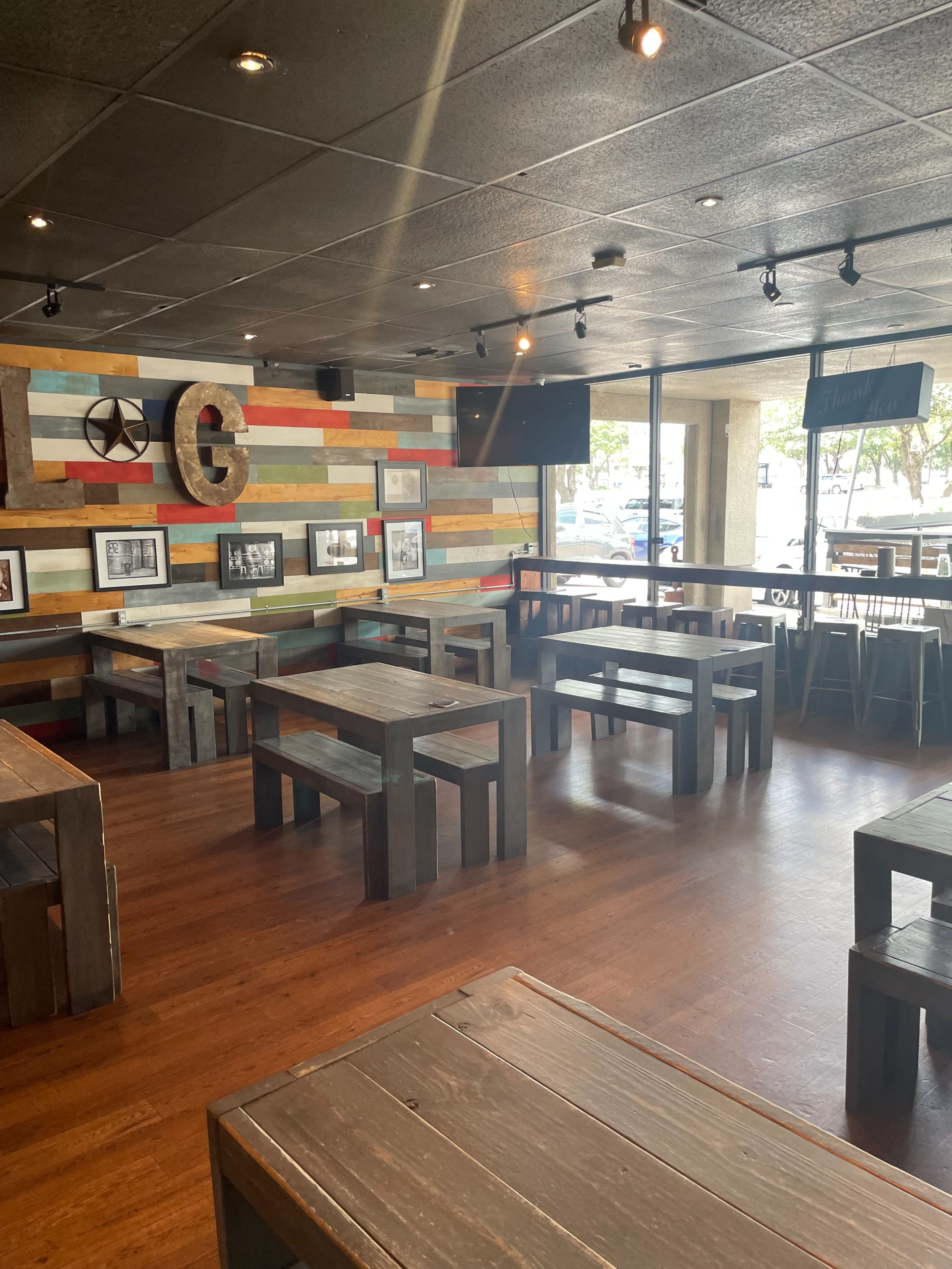 An empty modern restaurant with wooden tables and a colorful accent wall featuring framed photographs.