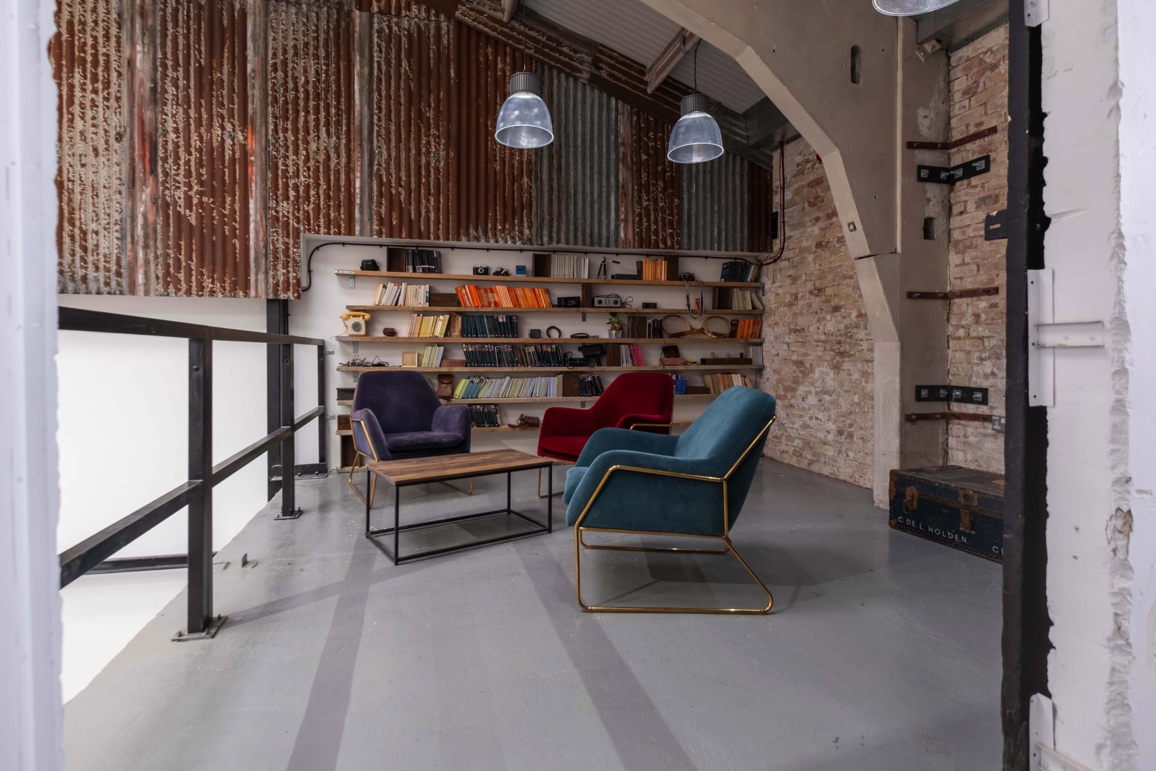 A stylish room features three chairs and a bookshelf against a textured wall made of metal and brick.