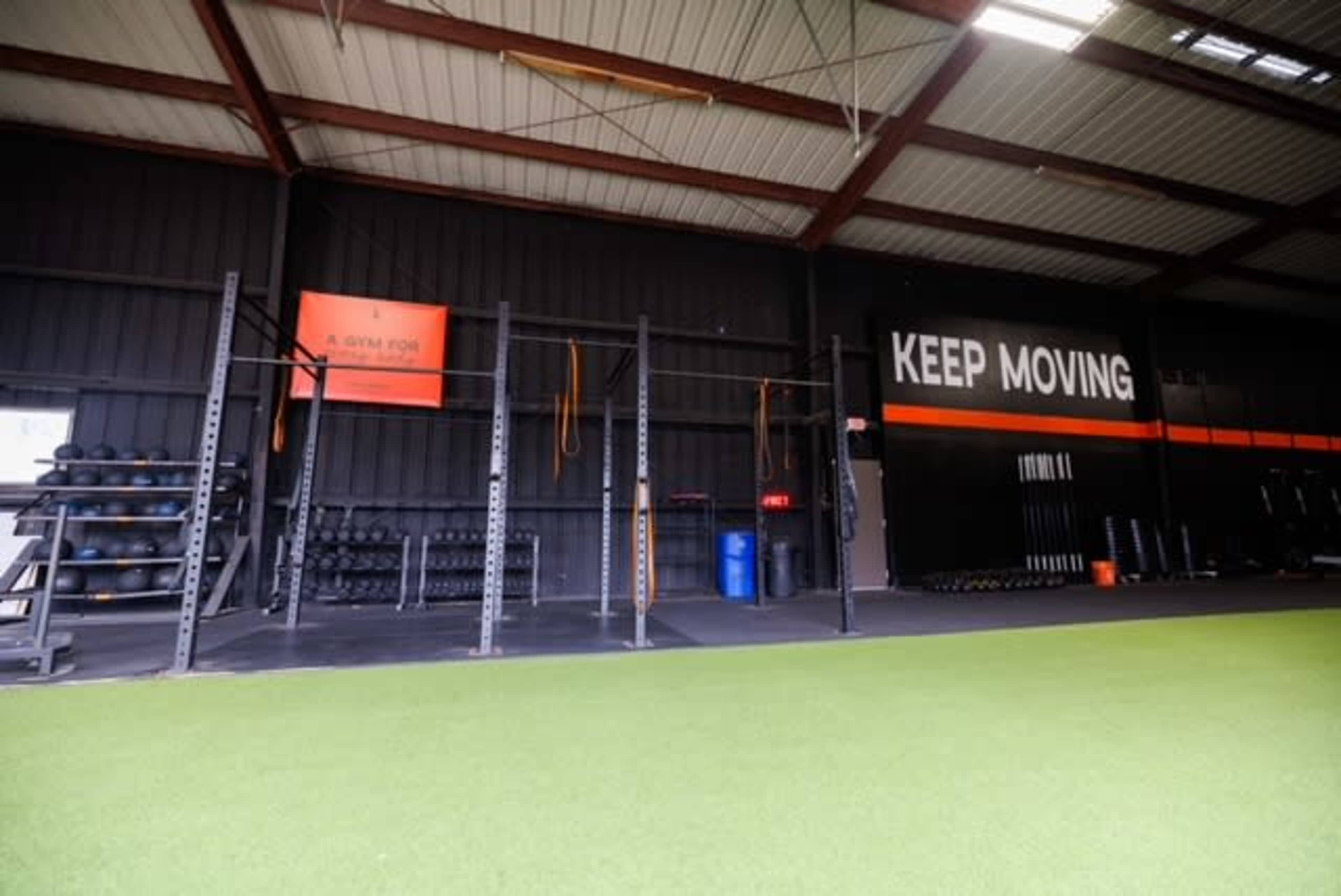 A gym interior with workout equipment, including weights and a pull-up rig, alongside a motivational slogan on the wall.