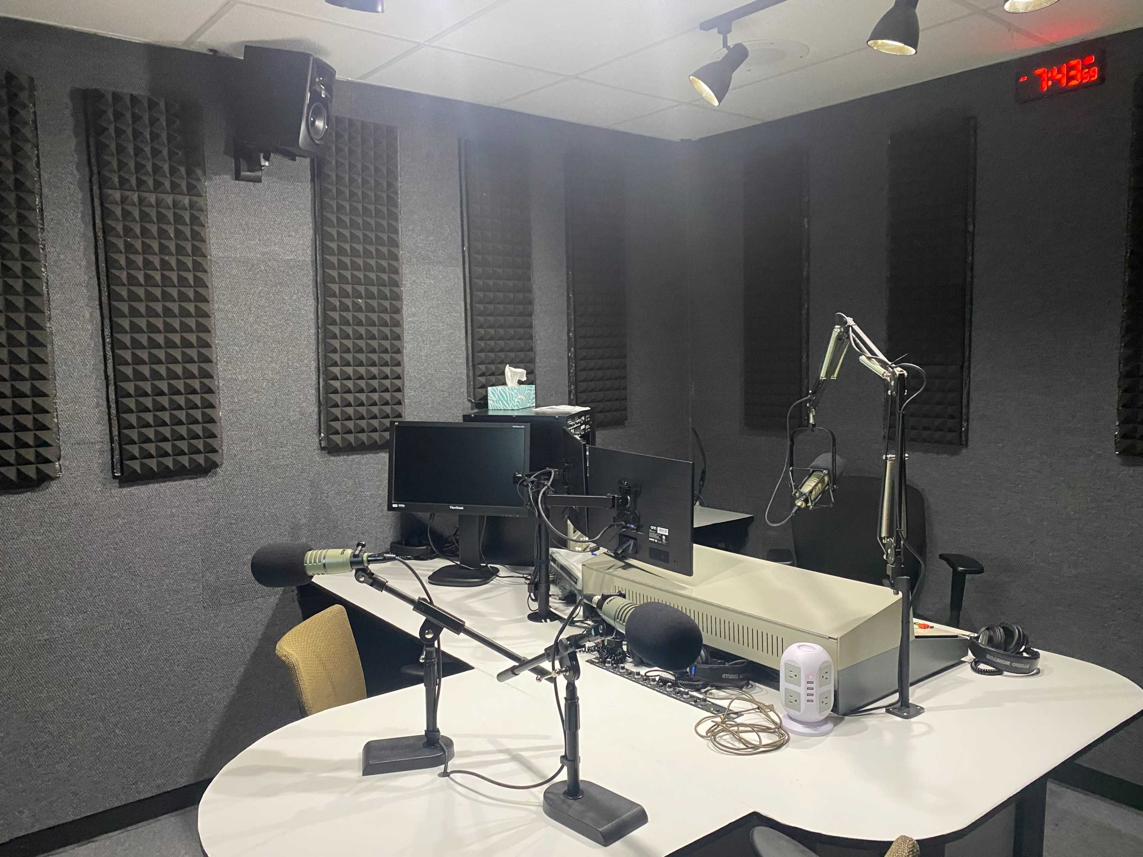 A soundproof recording studio with a central table, microphones, and computer monitors.