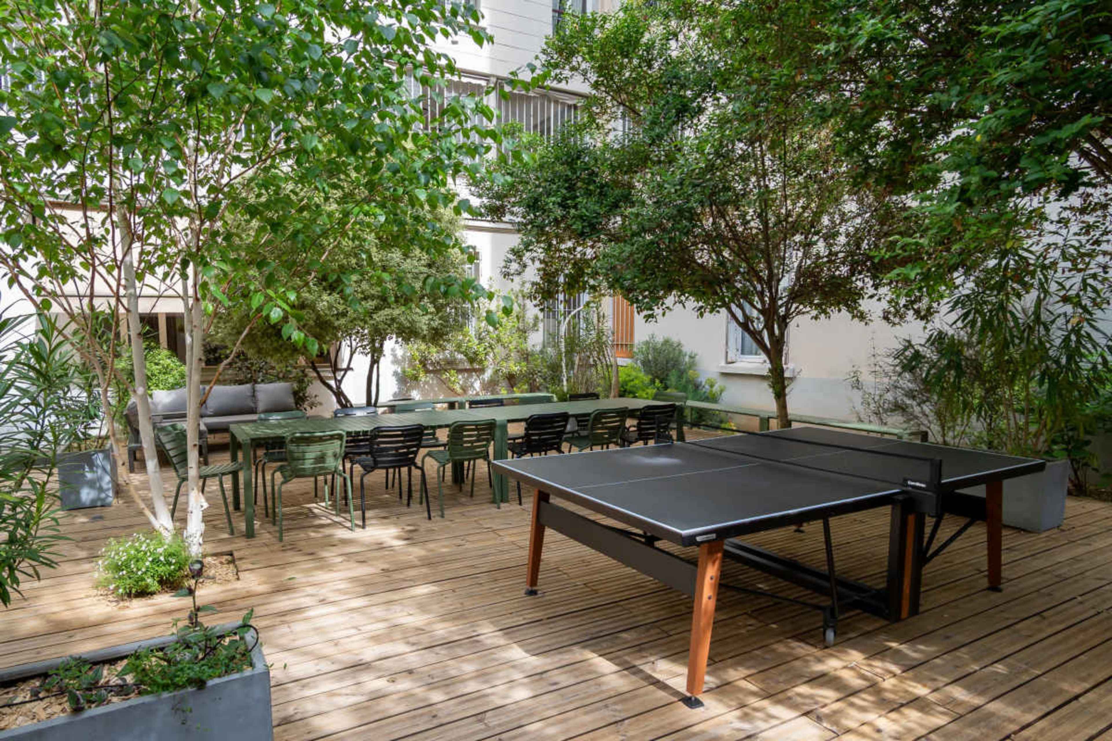 The scene features a wooden deck with a ping pong table and a dining area surrounded by lush greenery.