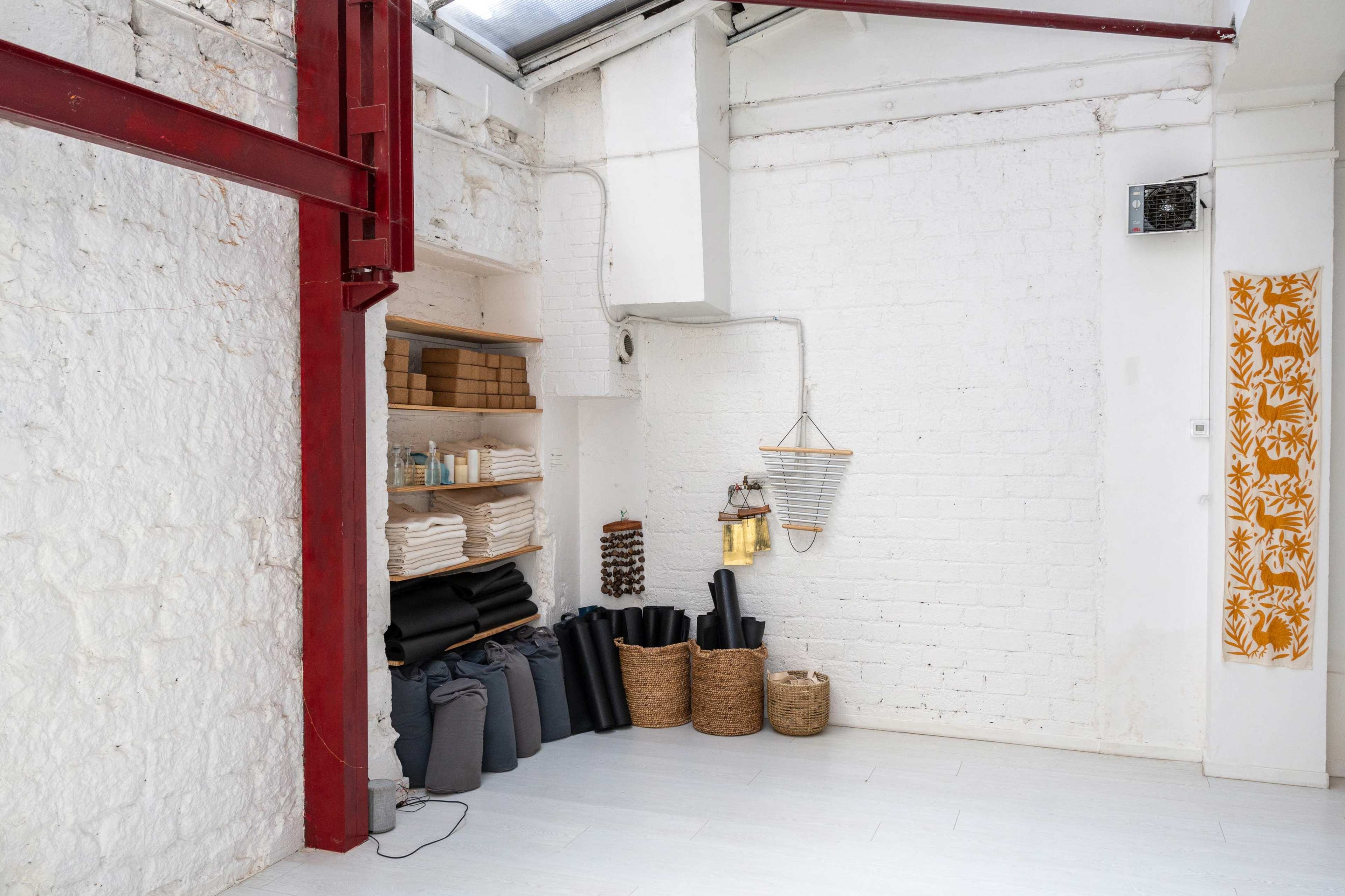 The image shows a bright, minimalistic room with white walls, shelves holding neatly stacked towels, and decorative items including woven baskets and a lantern.