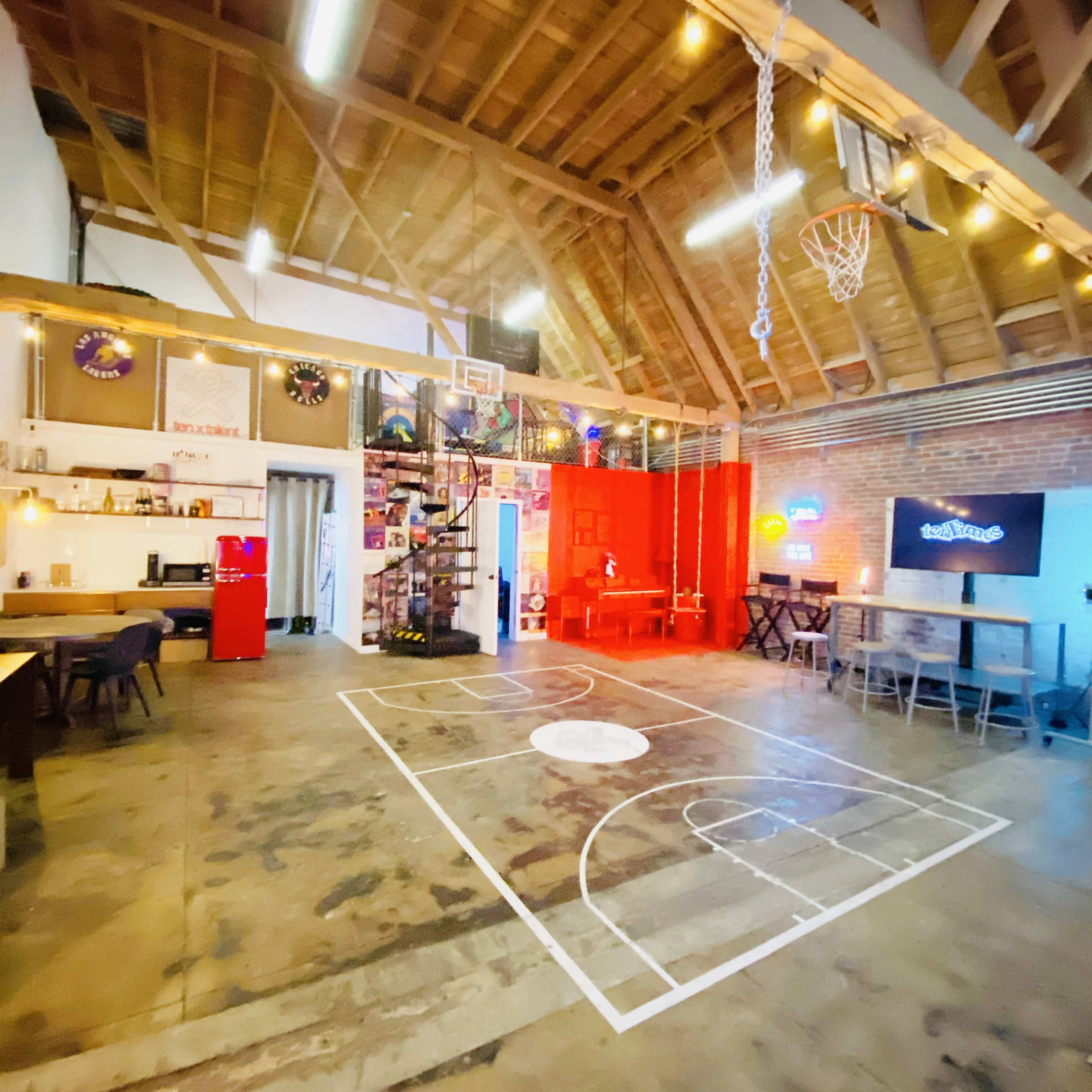 A spacious, industrial-style room with a basketball court design on the floor, featuring a basketball hoop and various seating arrangements.