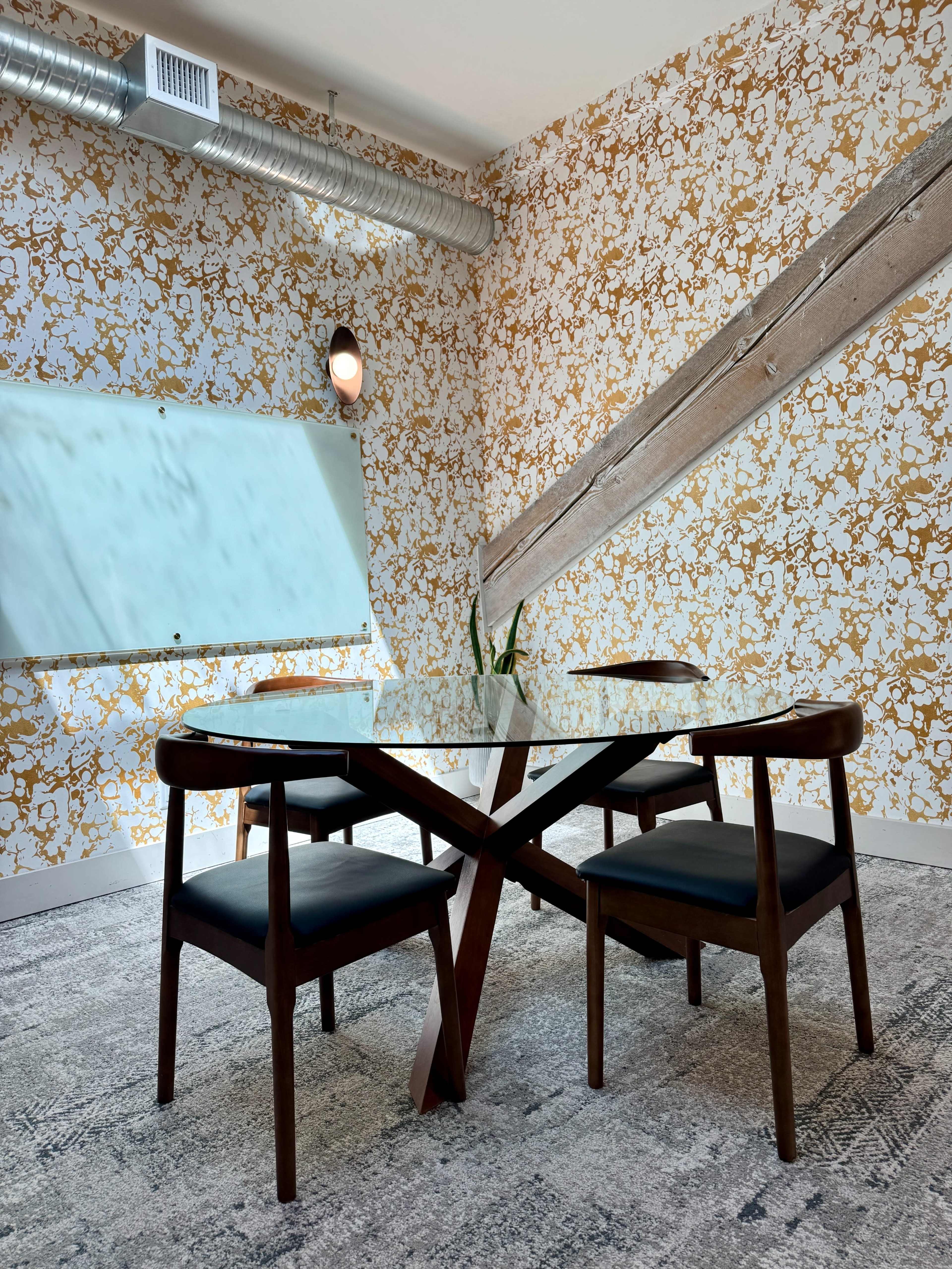 The image shows a modern meeting room with a glass table, two wooden chairs, and a decorative wall featuring floral patterns.