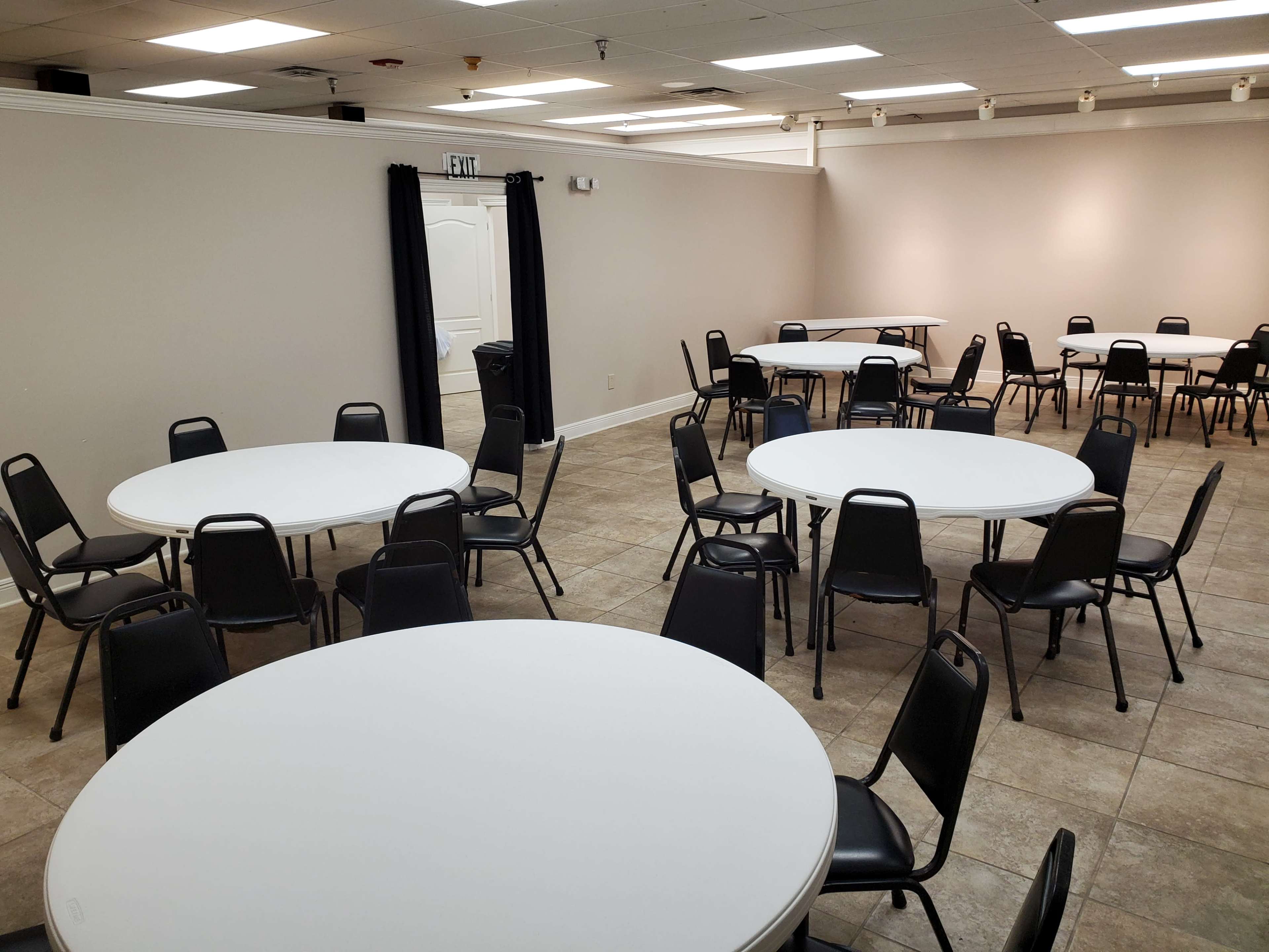 A spacious room with several round tables and black chairs arranged around them.