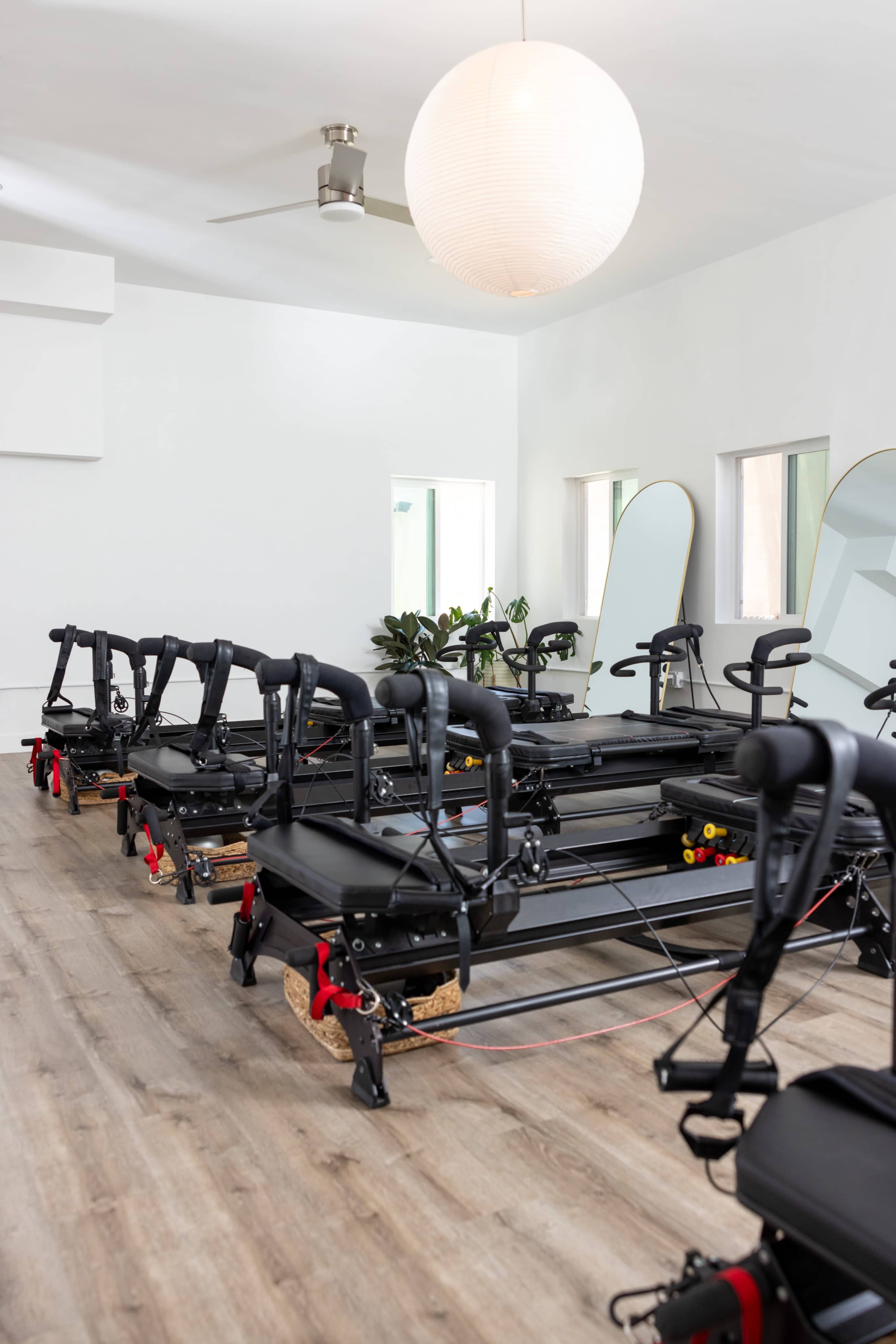 The image shows a fitness studio with several reformer machines neatly arranged on a wooden floor.
