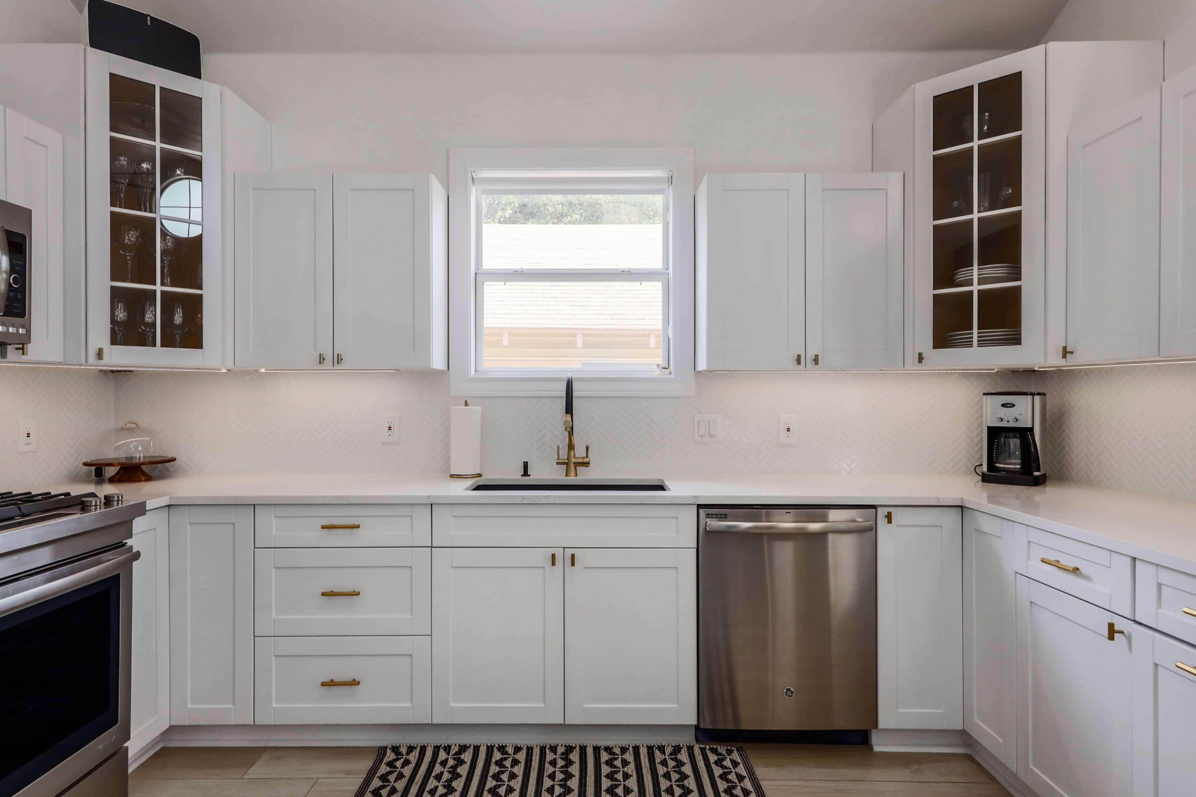 A modern kitchen featuring white cabinetry, a stainless steel dishwasher, and a sink positioned beneath a window.