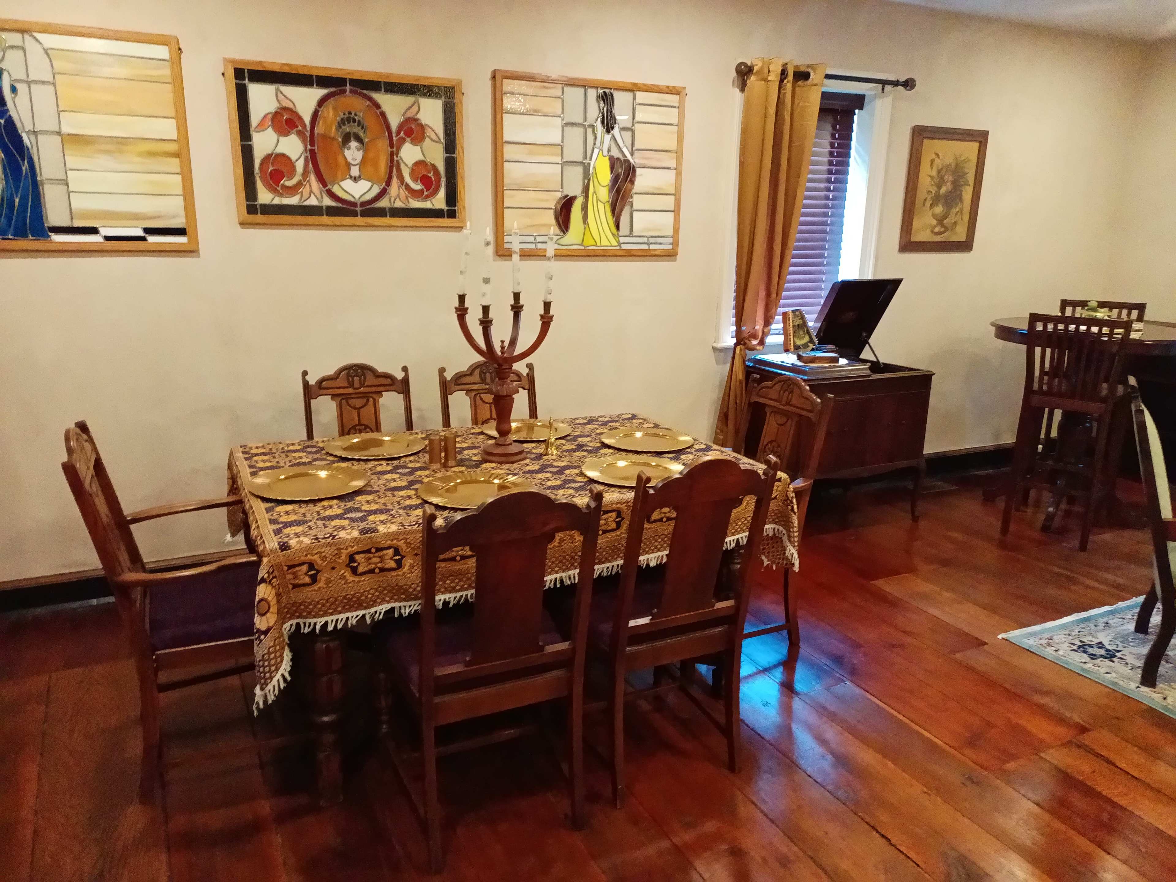 A wooden dining table is set with plates and surrounded by five chairs in a room adorned with stained glass artwork and wooden furnishings.