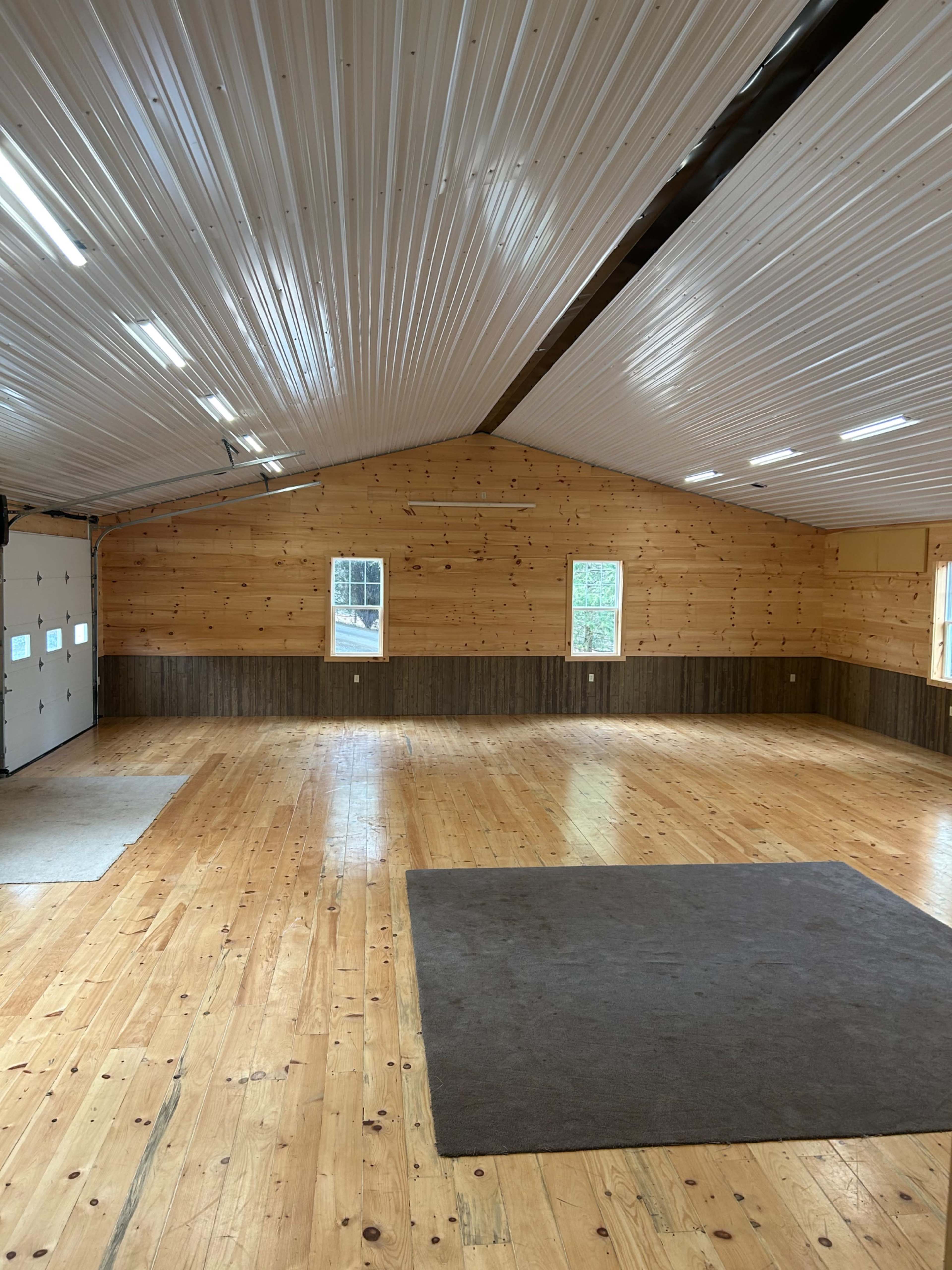 The interior of a spacious building features wooden walls, a high ceiling, and a polished wooden floor with minimal furnishings.
