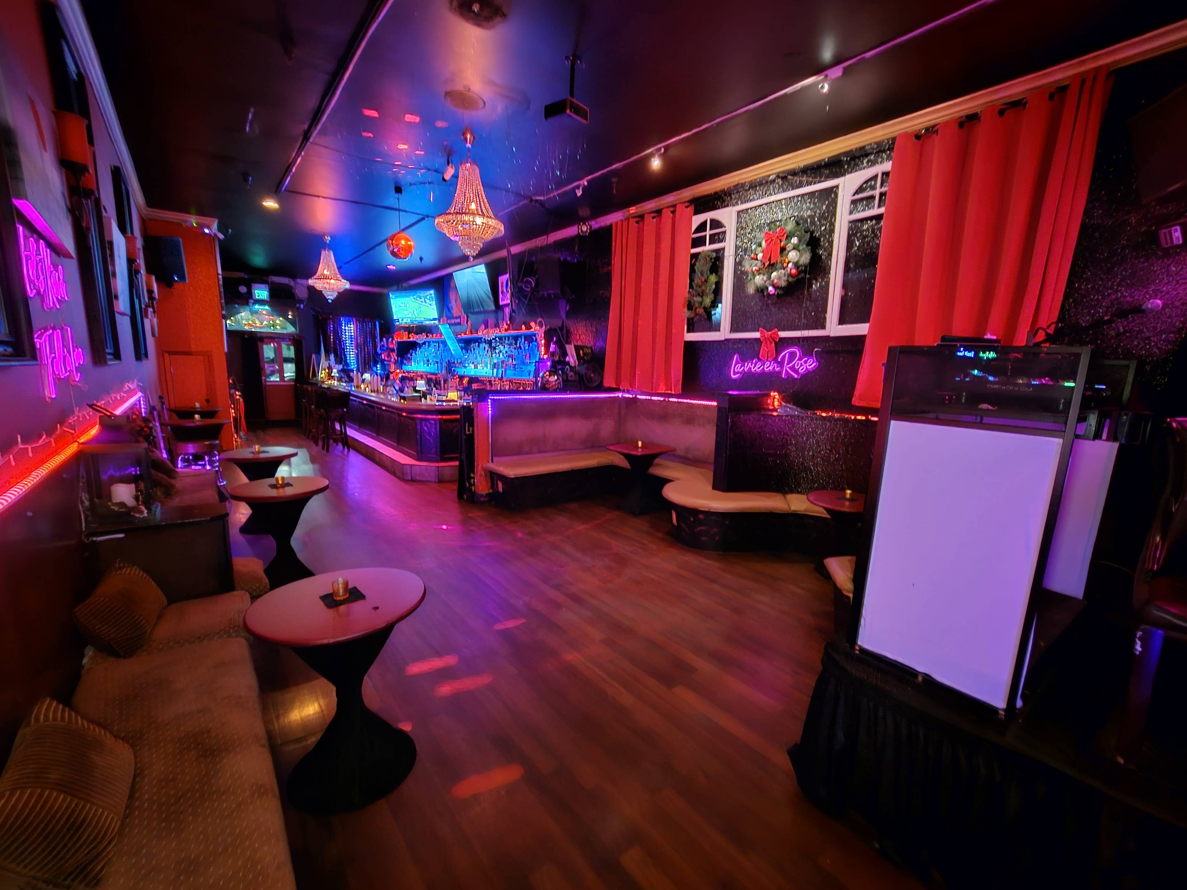 A dimly lit lounge with a bar area, seating along the walls, and colorful lighting.