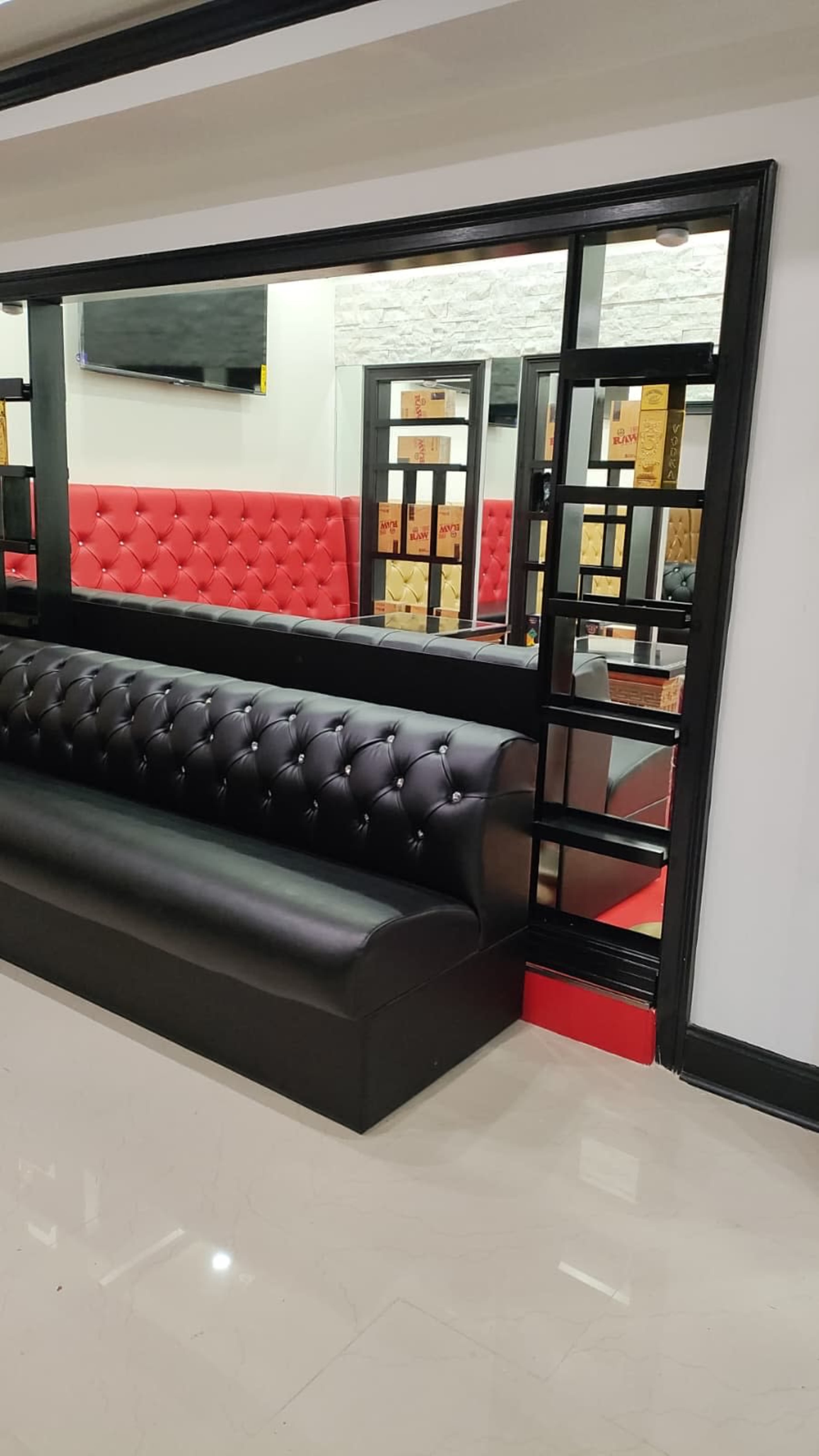 The image shows a modern interior with a black tufted bench, a large mirror, and red upholstered seating in the background.