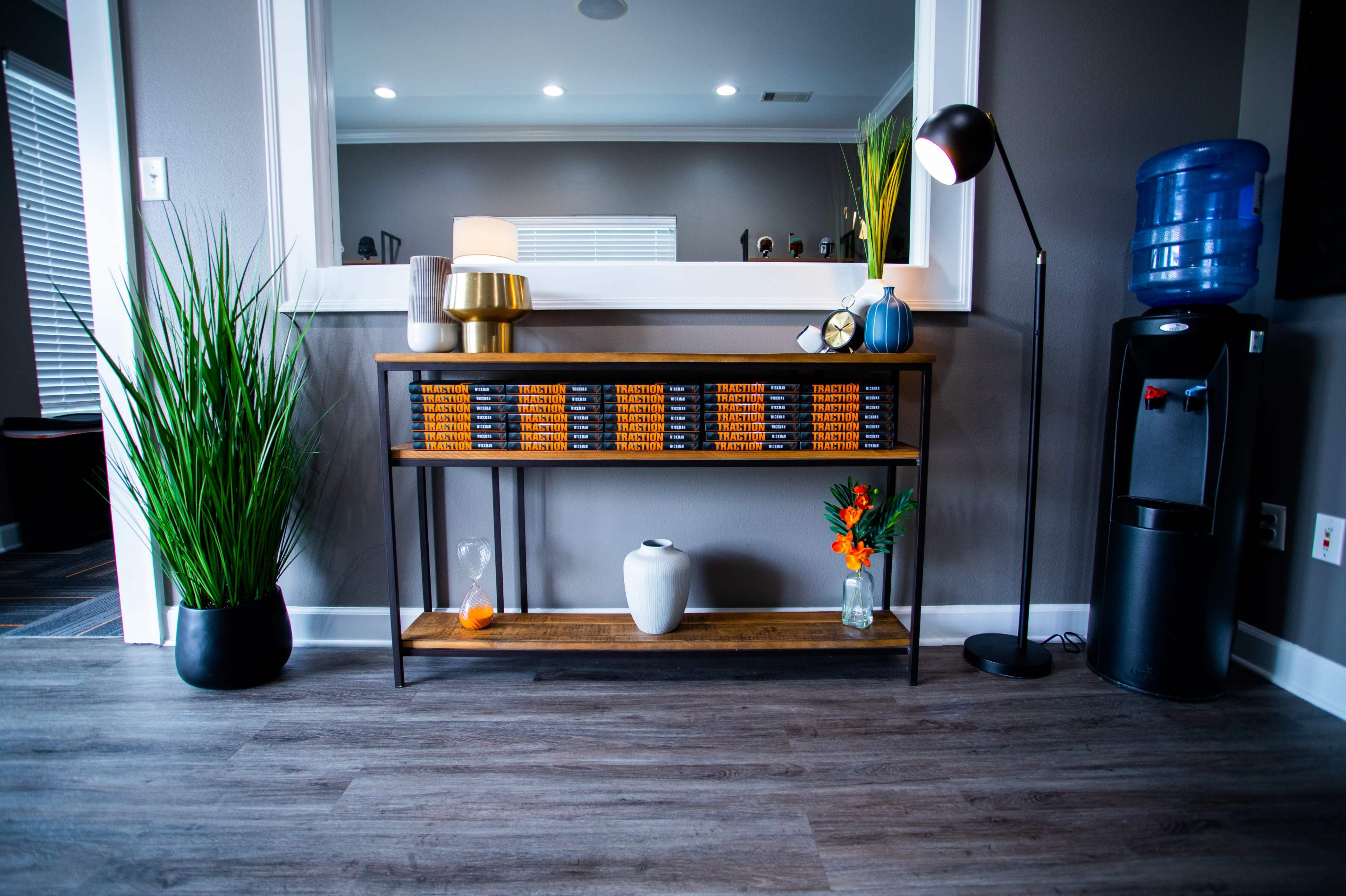 A modern console table with decorative objects and plants is positioned near a wall mirror in a well-lit room.