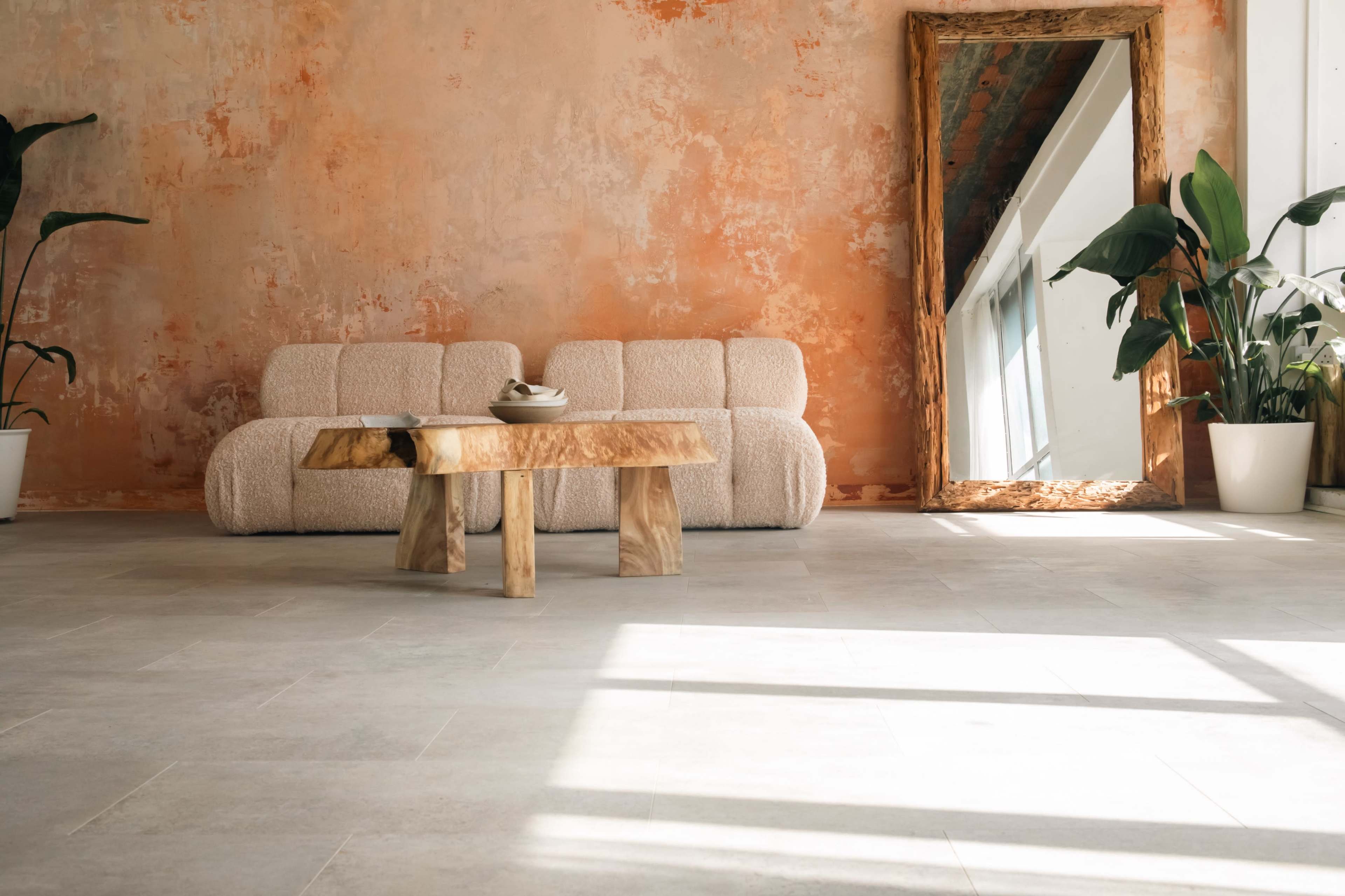 A cozy living space with a textured orange wall, a light-colored couch, a wooden coffee table, and potted plants.
